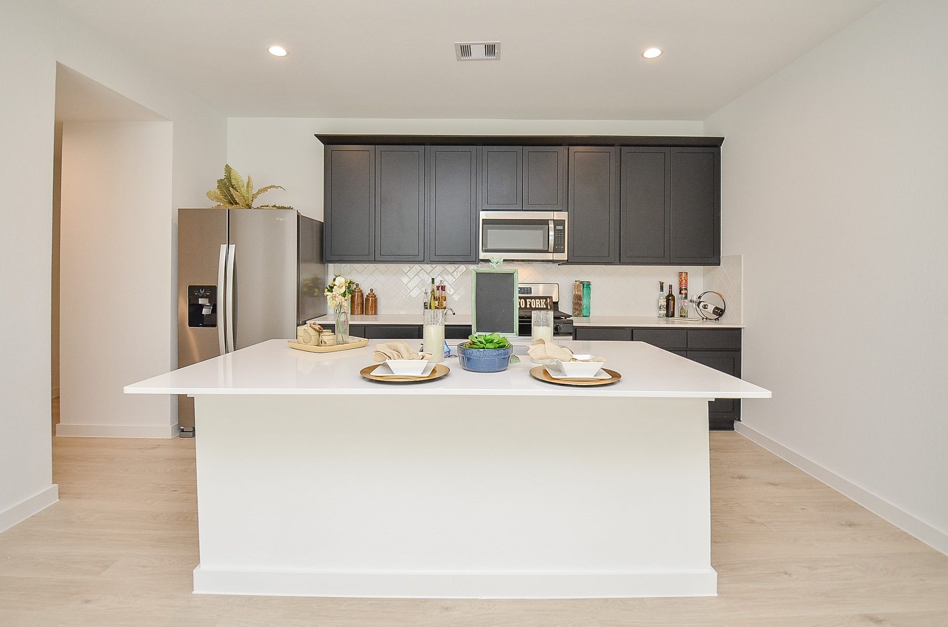 7814 Bel Fiore Drive, Richmond, TX 77406 Sleek modern kitchen featuring a spacious island with elegant countertops, dark cabinetry, stainless steel appliances, and stylish accents for a contemporary feel.