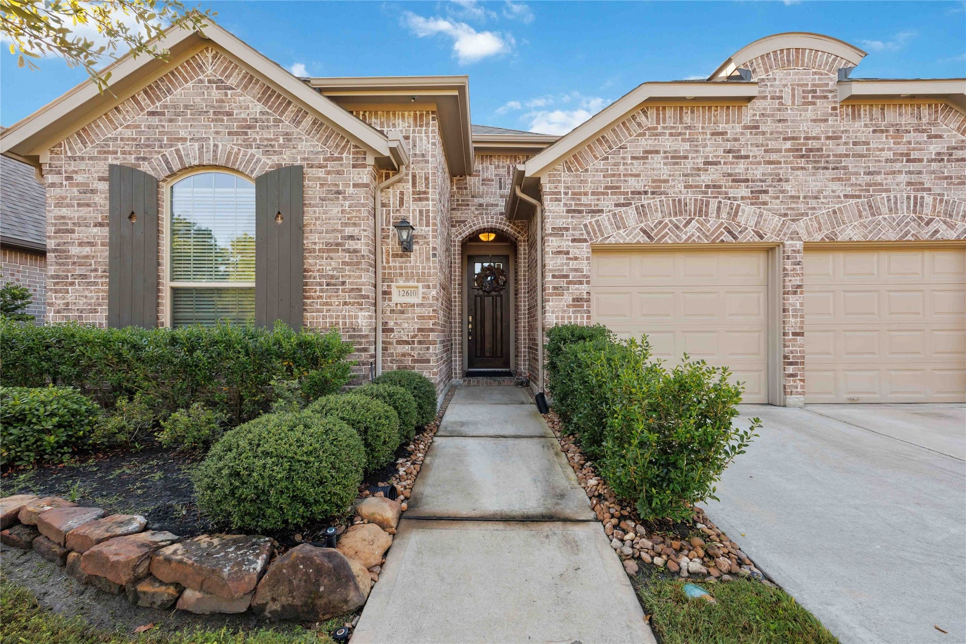 12610 Woodbourne Forest Drive, Humble, TX 77346 This beautiful home features a charming brick exterior with arched windows and a welcoming pathway leading to the front door. Well-maintained landscaping enhances its curb appeal, and the two-car garage offers ample parking space.