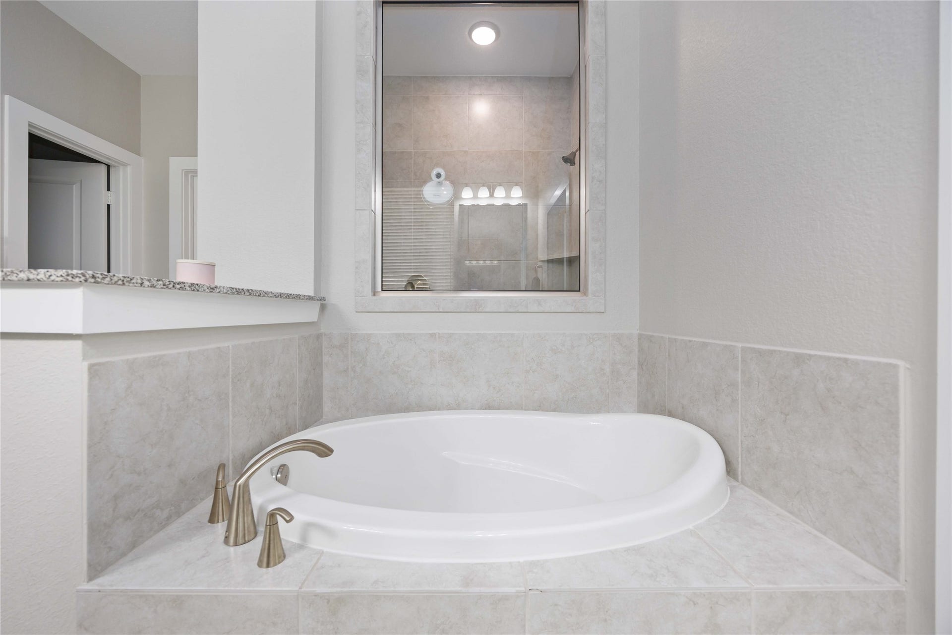 12610 Woodbourne Forest Drive, Humble, TX 77346 This bathroom features a modern, corner oval bathtub with sleek fixtures, surrounded by light beige tiles, creating a clean and elegant look.
