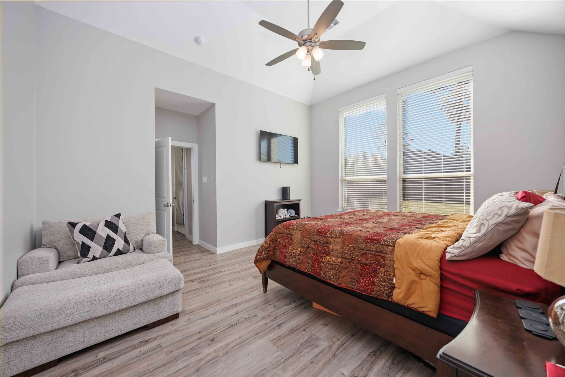 12610 Woodbourne Forest Drive, Humble, TX 77346 This bedroom is bright and spacious, featuring large windows, a ceiling fan, and light-colored flooring. It includes a cozy sitting area, mounted TV, and a comfortable bed, creating a welcoming and functional space.