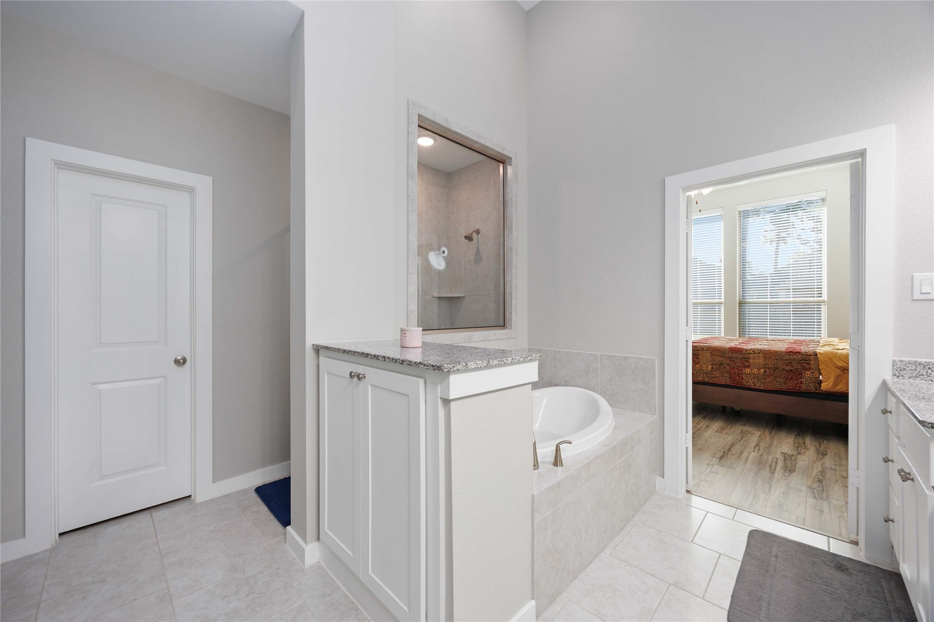12610 Woodbourne Forest Drive, Humble, TX 77346 This bathroom features a modern design with a corner bathtub, separate shower, and neutral tile flooring. It connects to a bedroom with large windows, offering plenty of natural light.