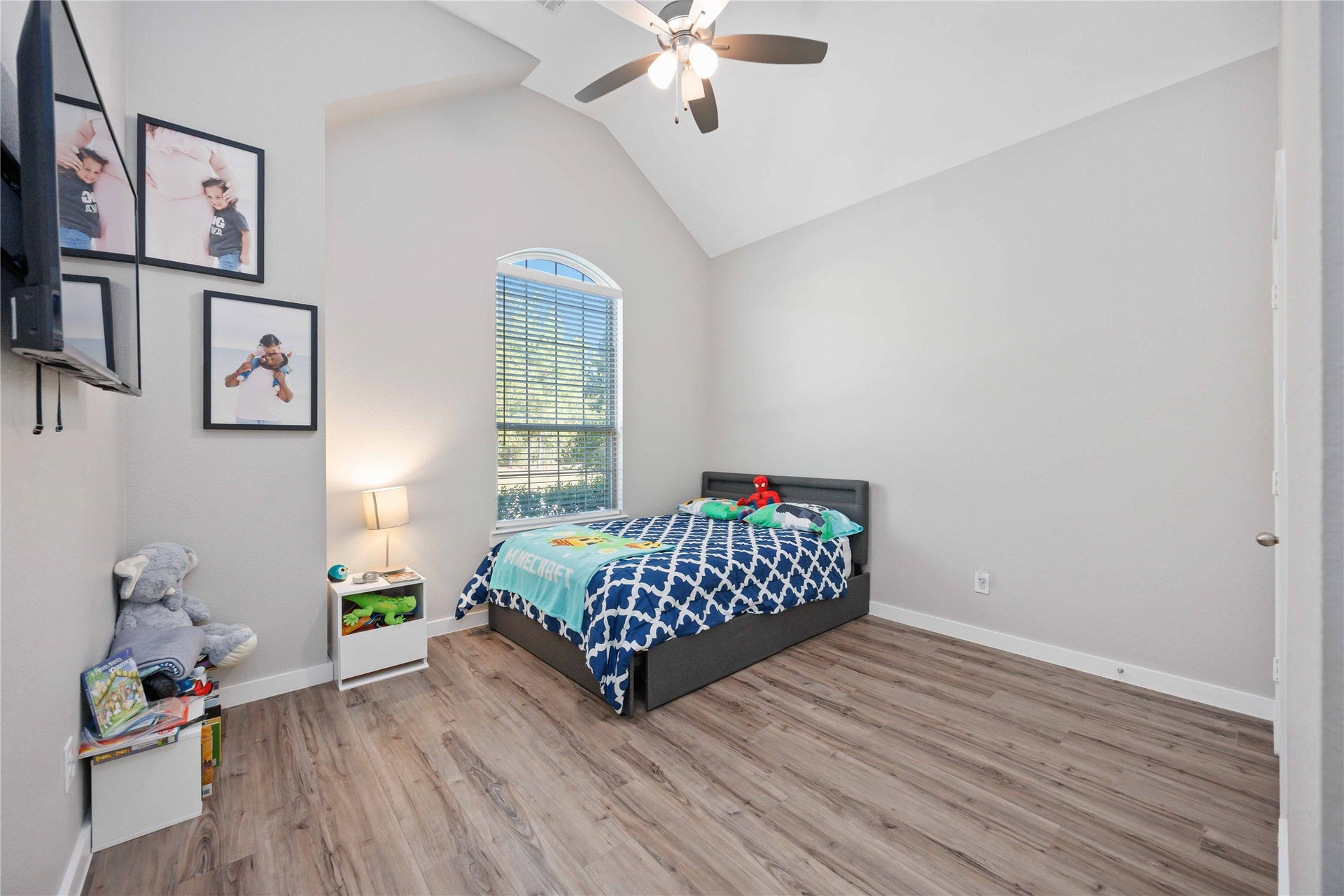 12610 Woodbourne Forest Drive, Humble, TX 77346 This bedroom features high ceilings and abundant natural light from a large, arched window. The room has wood-style flooring, a ceiling fan, and neutral walls, offering a modern and spacious feel. Its ideal for a child's room with playful decor and ample space for a bed and furniture.