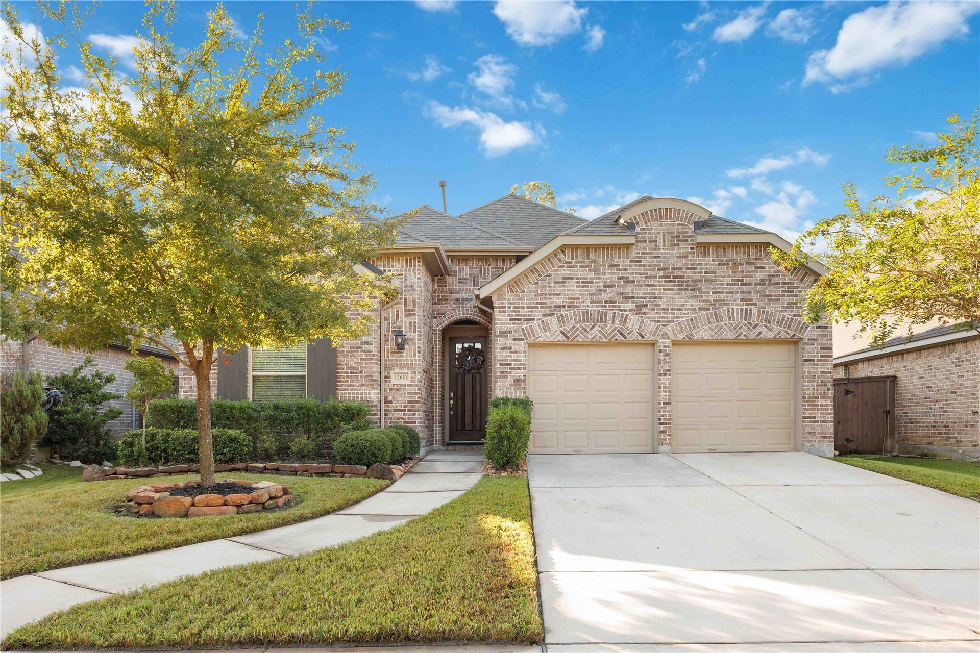 12610 Woodbourne Forest Drive, Humble, TX 77346 This charming home features a welcoming brick exterior, a two-car garage, and a neatly landscaped front yard with a well-maintained lawn and mature trees. The pathway leads to an elegant front door, creating a warm and inviting entrance.