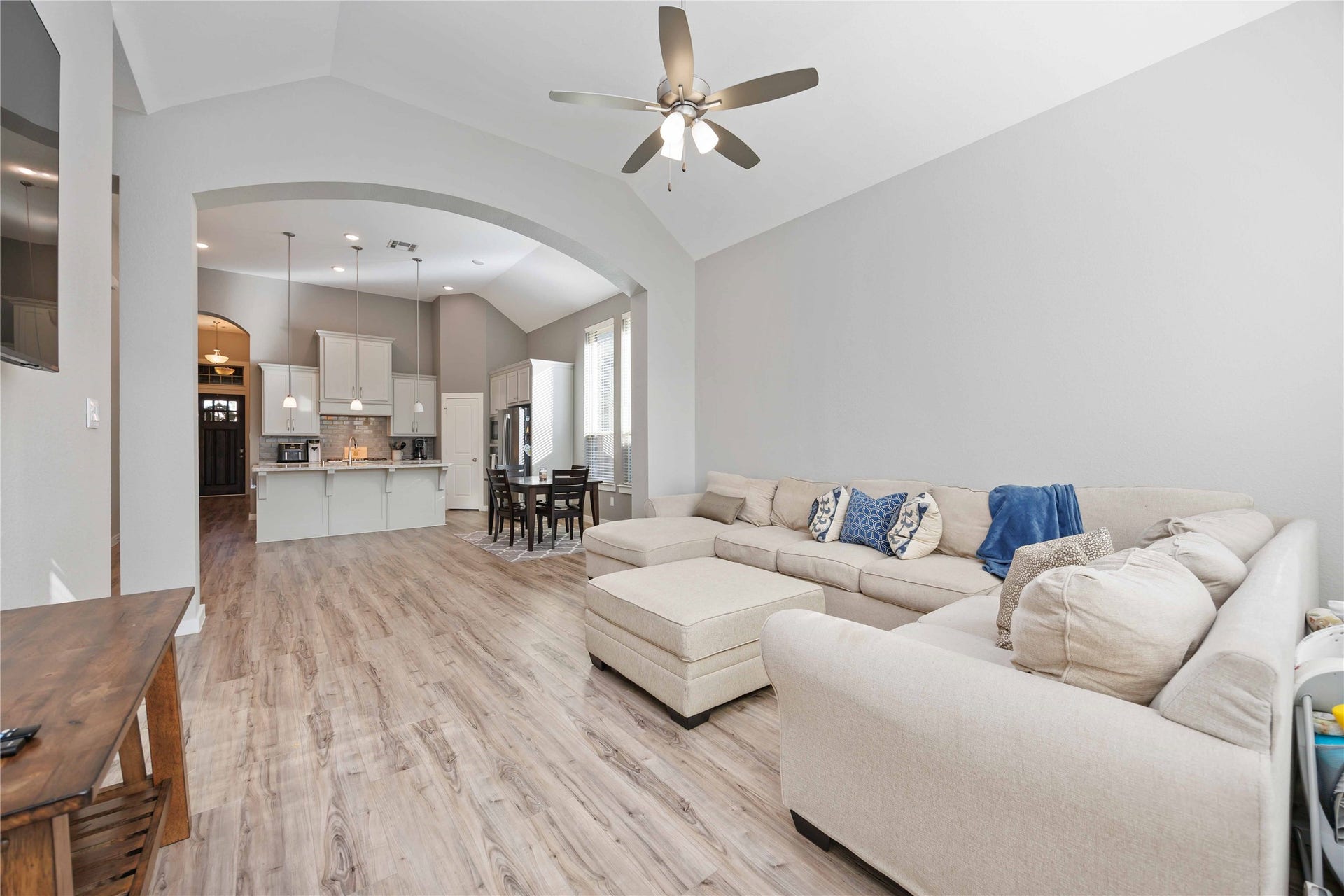 12610 Woodbourne Forest Drive, Humble, TX 77346 This inviting open-concept living space features a cozy beige sectional, vaulted ceilings, and wood-look flooring. It seamlessly connects to a modern kitchen with a breakfast bar and a dining area, offering a spacious and airy feel. Perfect for family gatherings and entertaining.