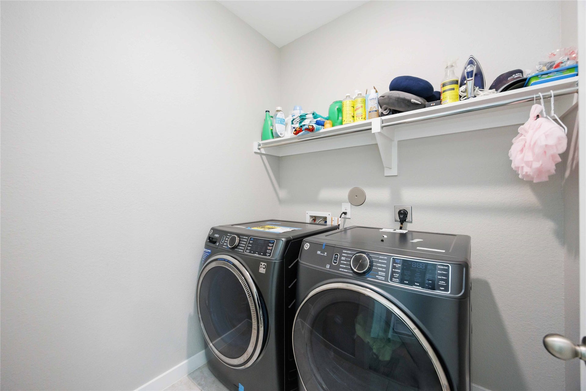 12610 Woodbourne Forest Drive, Humble, TX 77346 This laundry room features modern black front-loading washer and dryer units. It has a wall-mounted shelf for storage, ideal for organizing cleaning supplies. The space is bright and functional.