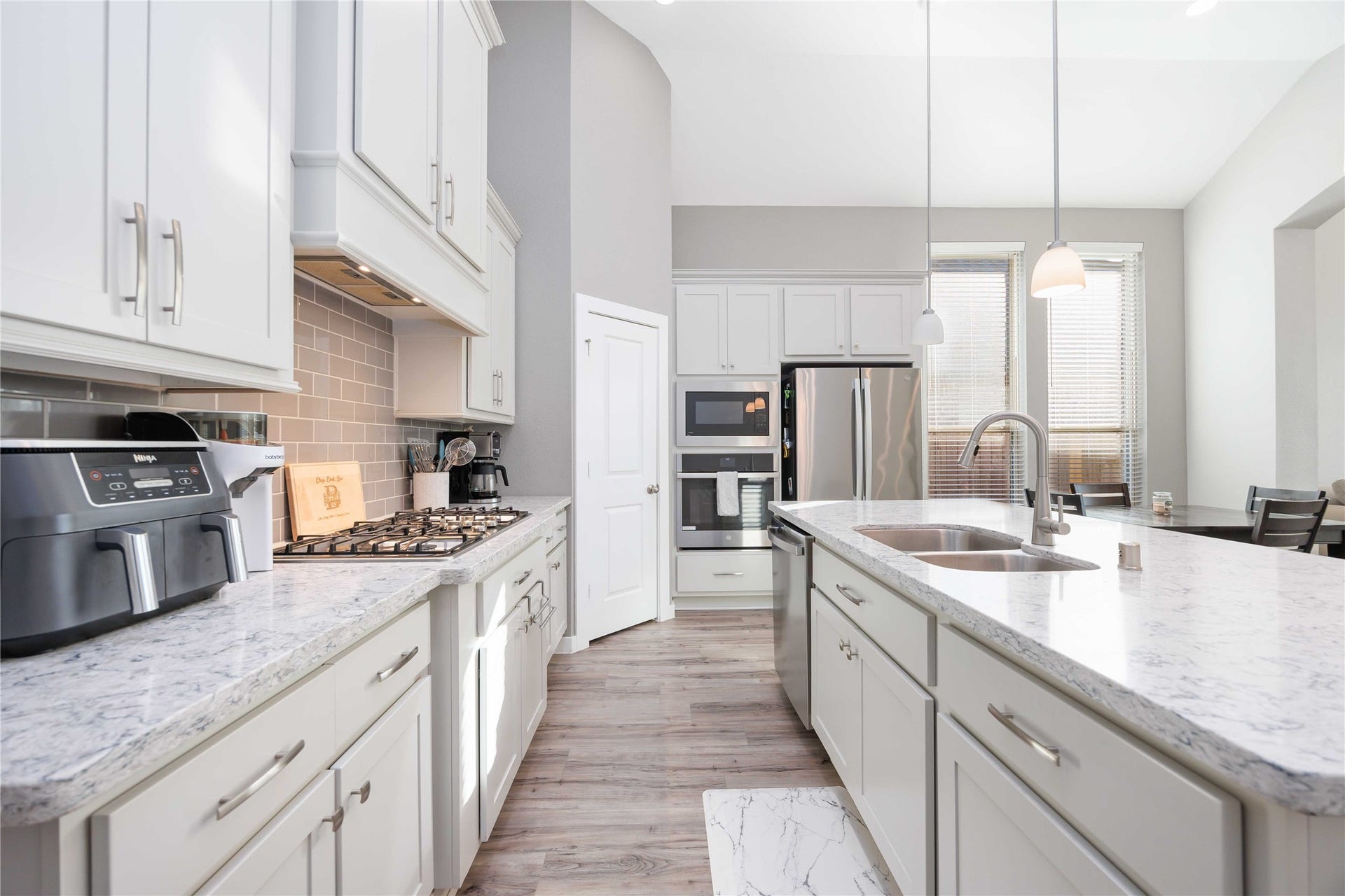 12610 Woodbourne Forest Drive, Humble, TX 77346 This modern kitchen features sleek white cabinetry, granite countertops, and stainless steel appliances. It includes a spacious island with a double sink, pendant lighting, and a gas stove, offering a bright, open feel with ample natural light.