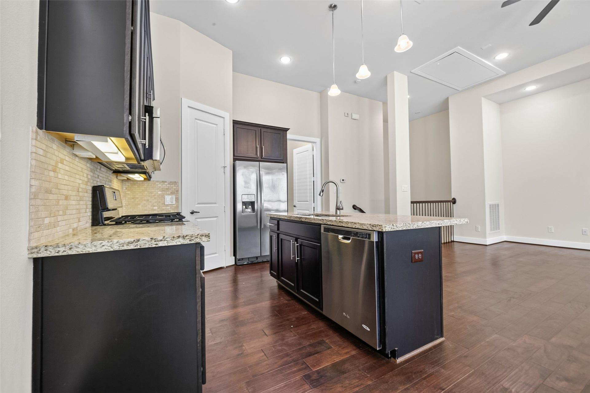 40 N Hutcheson Street, Houston, TX 77003 Spacious kitchen with sleek dark cabinetry, granite countertops, and modern stainless steel appliances, seamlessly opening into a bright living area with elegant hardwood floors.