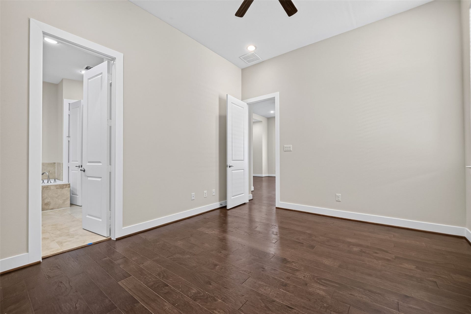 40 N Hutcheson Street, Houston, TX 77003 Spacious room with elegant hardwood floors and neutral walls, featuring a ceiling fan and access to a tiled bathroom with a soaking tub.