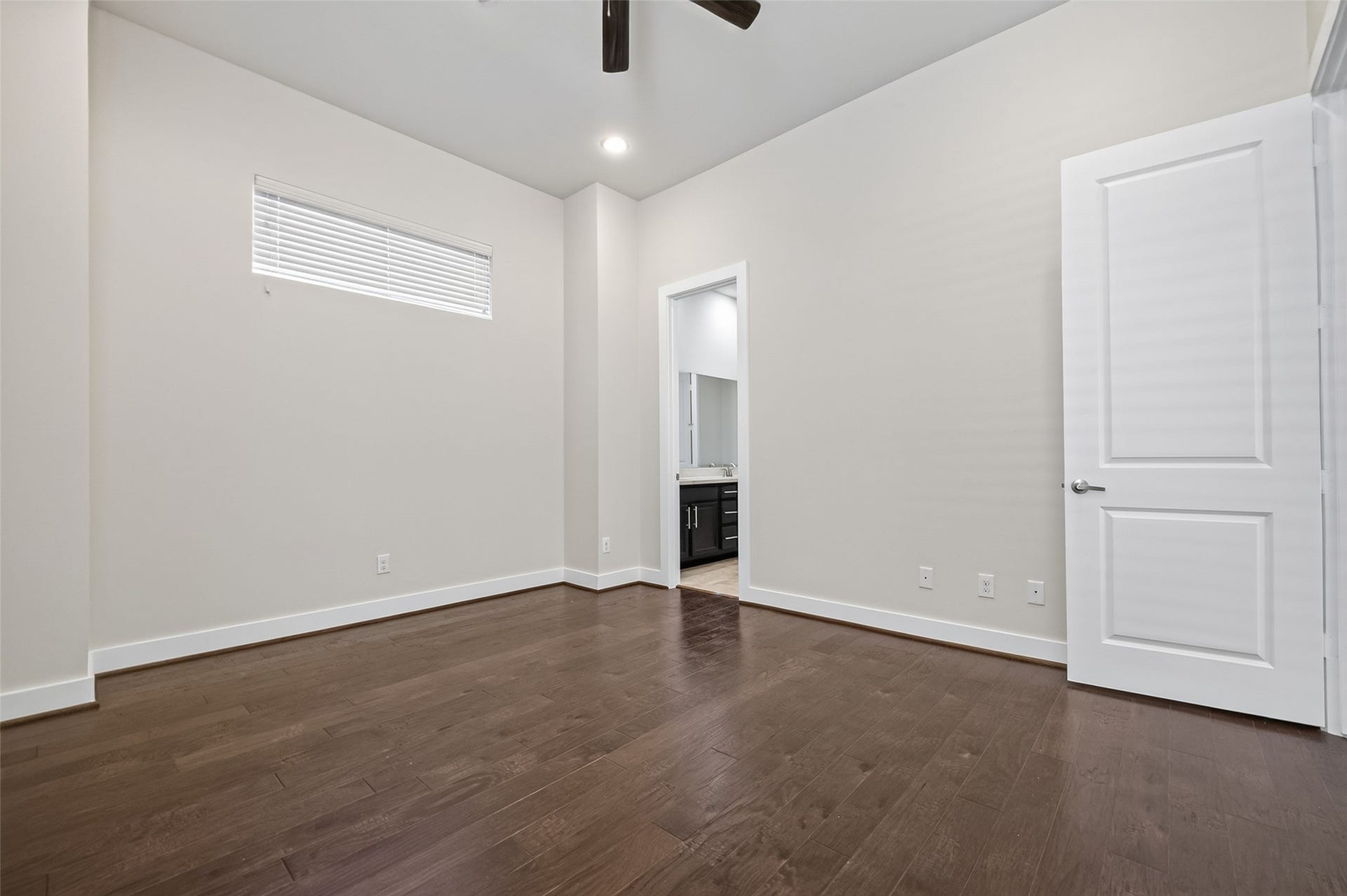 40 N Hutcheson Street, Houston, TX 77003 Spacious bedroom with hardwood floors, neutral walls, and a ceiling fan, leading to an en-suite bathroom.