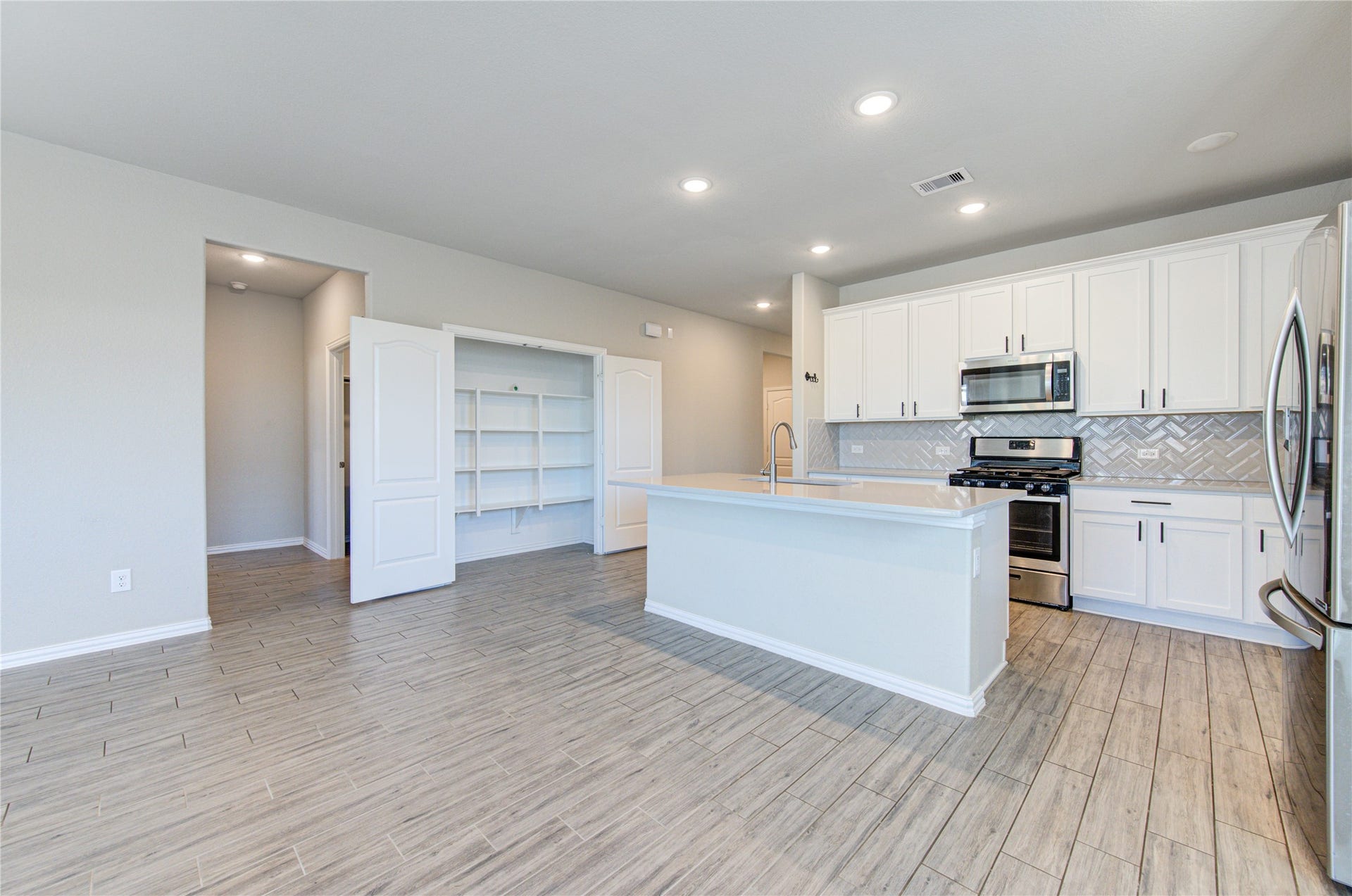 Bright, open kitchen with a large island, stainless steel appliances, ample cabinet space, and convenient built-in pantry storage