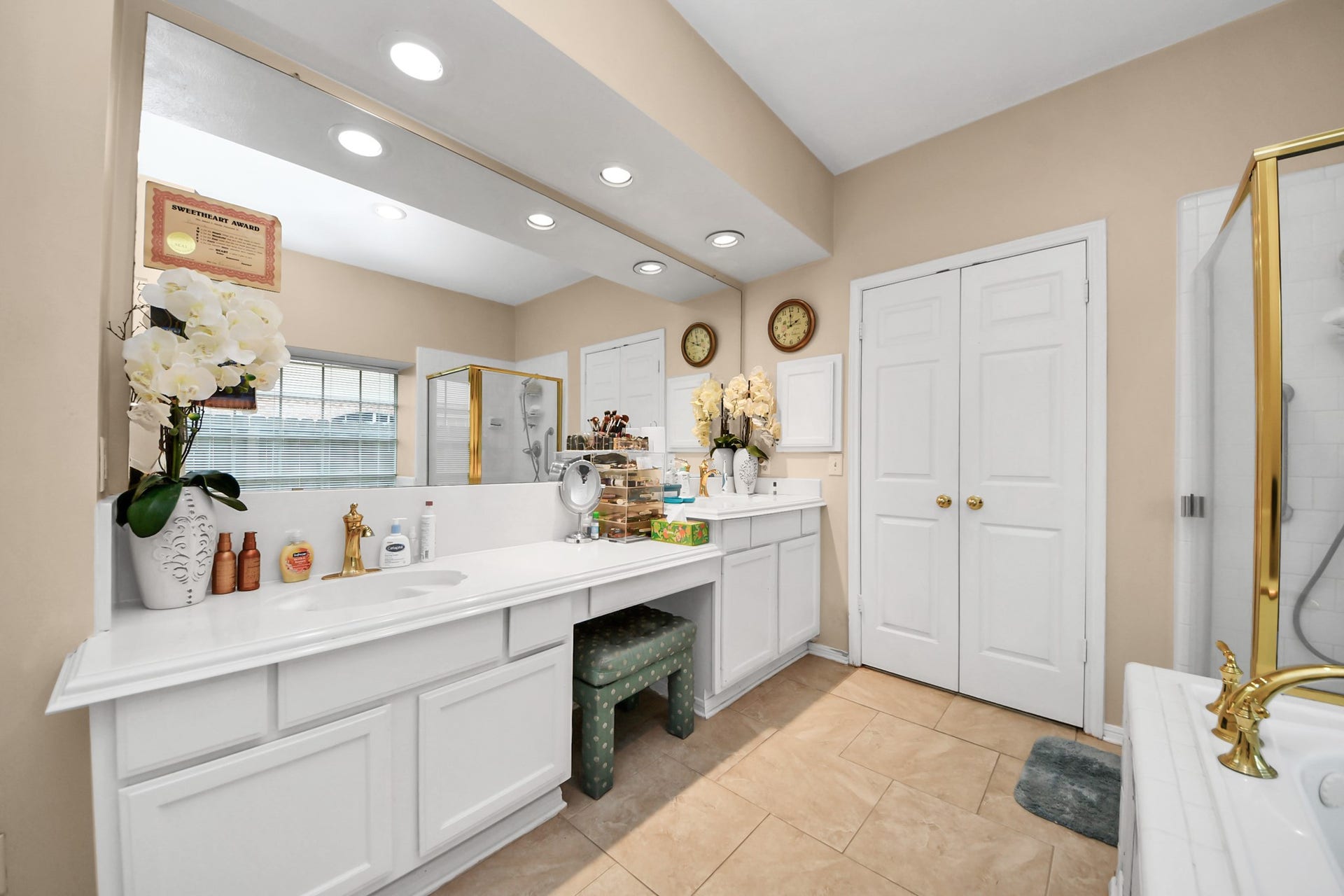 7015 Morningside Drive, Sugar Land, TX 77479 Spacious bathroom featuring dual sinks with ample counter space, elegant gold fixtures, and abundant natural light from a large window, complemented by tasteful decor.