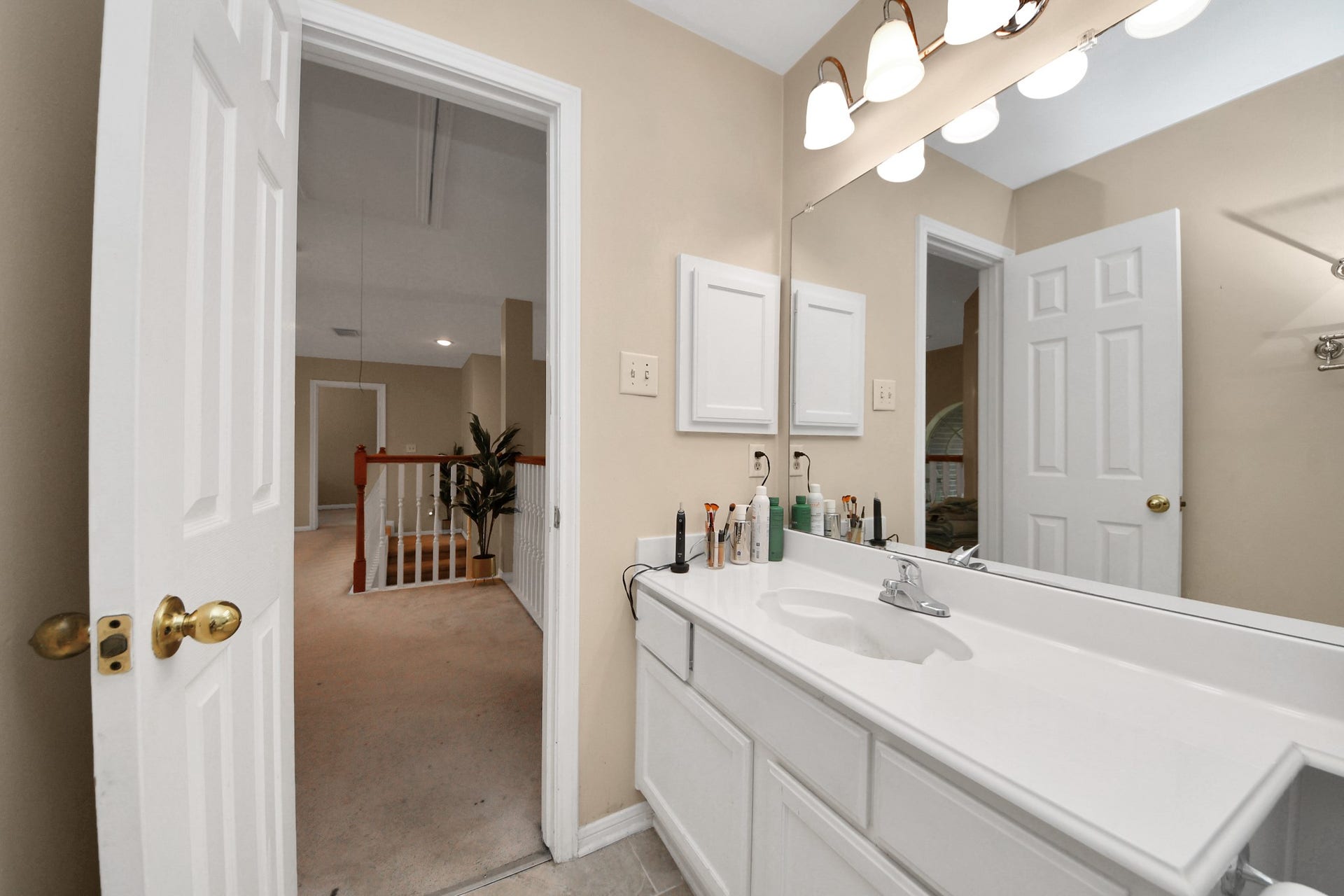 7015 Morningside Drive, Sugar Land, TX 77479 Bright bathroom with a spacious vanity and ample lighting, leading to a cozy carpeted hallway adorned with a decorative plant.
