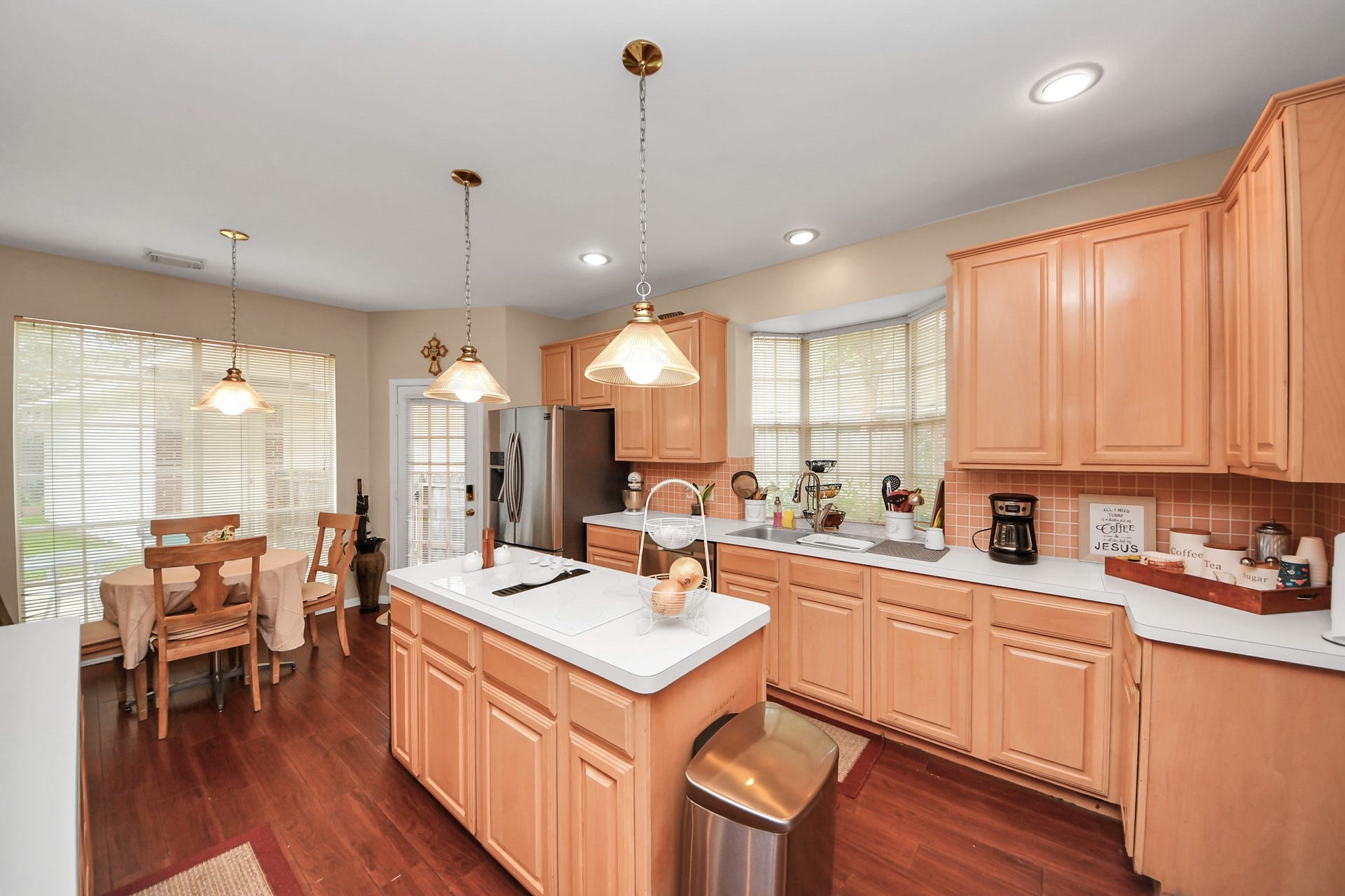 7015 Morningside Drive, Sugar Land, TX 77479 Spacious kitchen with warm wood cabinetry, modern stainless steel appliances, and a central island for meal preparation. The adjacent dining area is bathed in natural light from large windows, creating a welcoming space for gatherings.