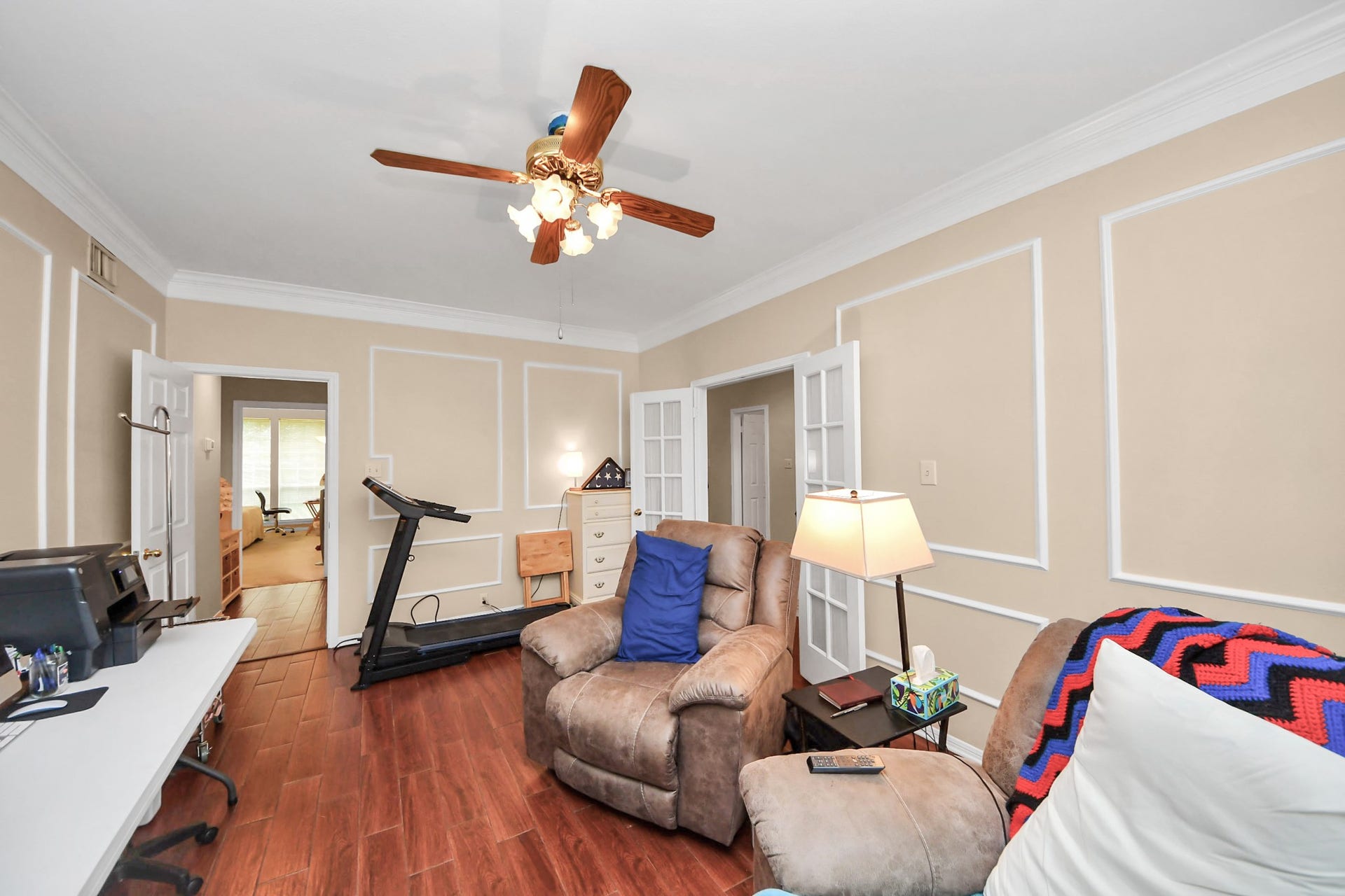 7015 Morningside Drive, Sugar Land, TX 77479 Cozy living area features elegant wall detailing, warm wood flooring, and a ceiling fan, offering a comfortable space perfect for relaxation and productivity.