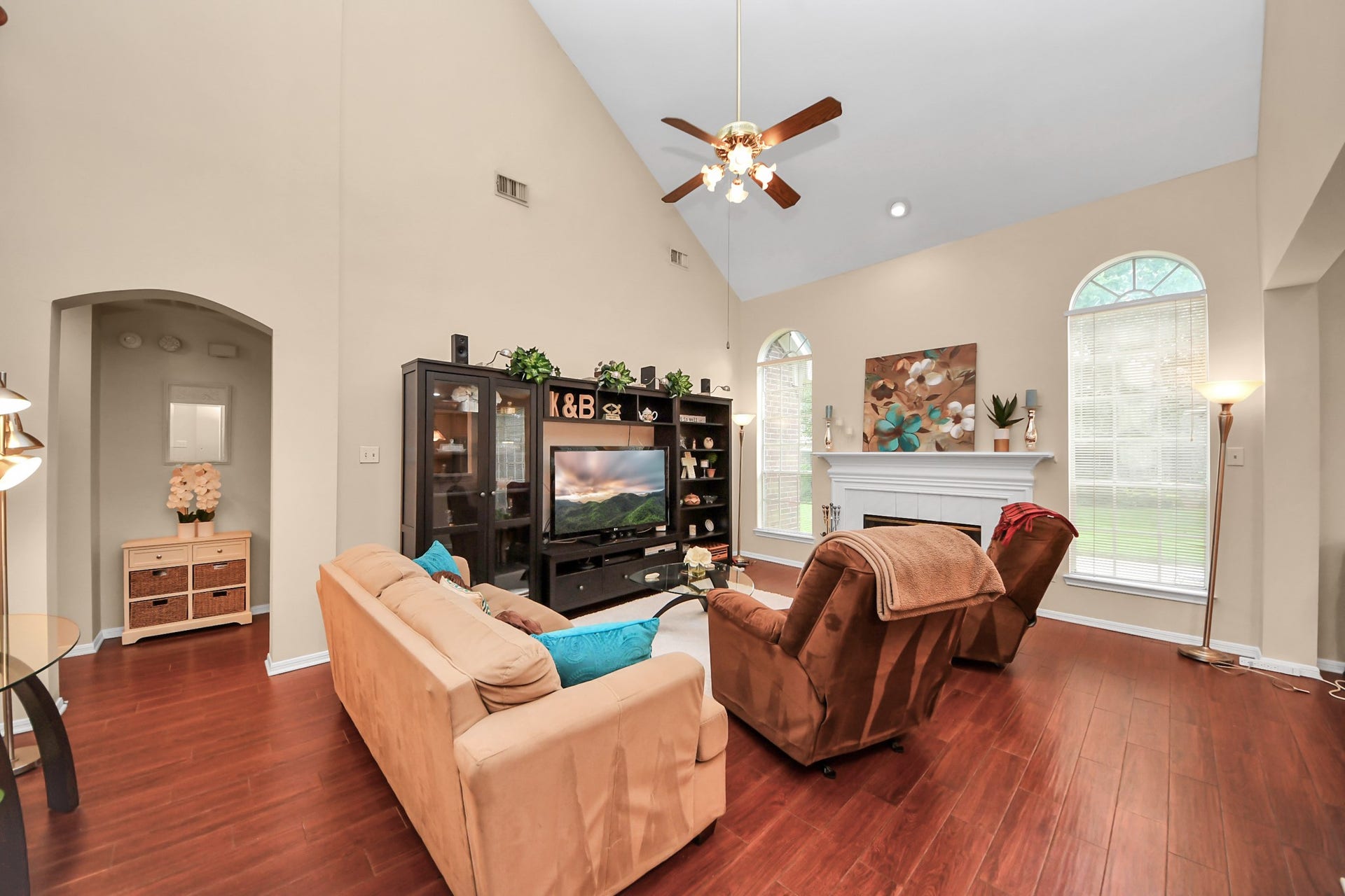 7015 Morningside Drive, Sugar Land, TX 77479 Spacious living room with vaulted ceilings, warm hardwood floors, and abundant natural light from arched windows, featuring a cozy fireplace and stylish entertainment center.