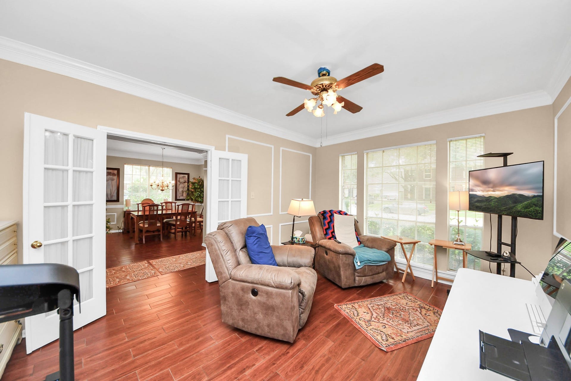 7015 Morningside Drive, Sugar Land, TX 77479 Bright and inviting living area with rich wood flooring, large windows for natural light, and elegant French doors leading to a spacious dining room.