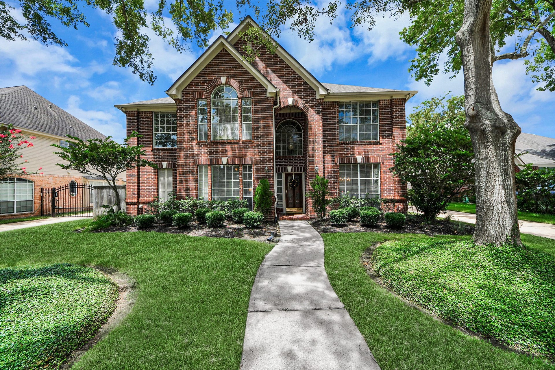 7015 Morningside Drive, Sugar Land, TX 77479 Stunning two-story brick home with elegant arched windows, surrounded by lush landscaping and mature trees, offering charming curb appeal in a serene neighborhood.