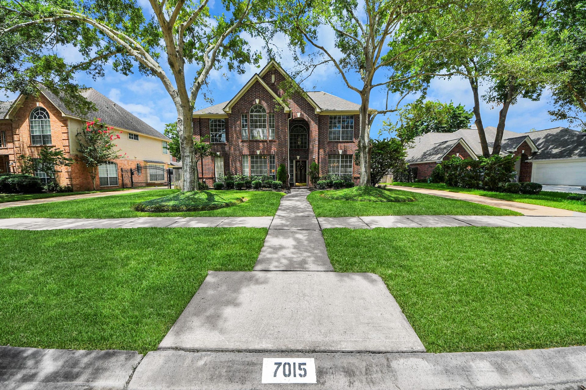 7015 Morningside Drive, Sugar Land, TX 77479 Charming two-story brick home with elegant arched windows, nestled in a serene neighborhood, featuring a beautifully manicured lawn and mature trees.