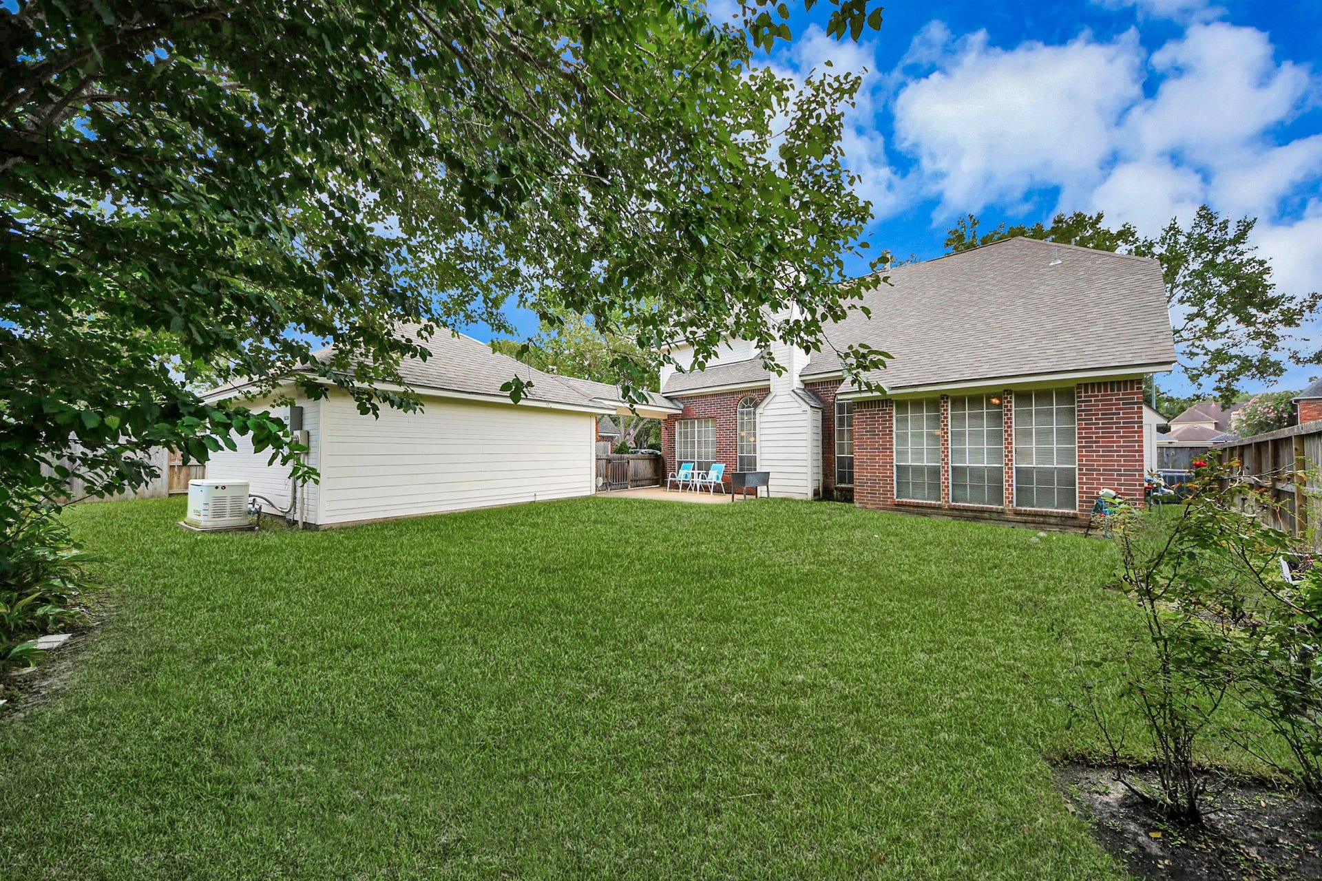 7015 Morningside Drive, Sugar Land, TX 77479 Spacious backyard with lush green lawn, mature trees, and a charming brick exterior, perfect for outdoor relaxation and entertainment.