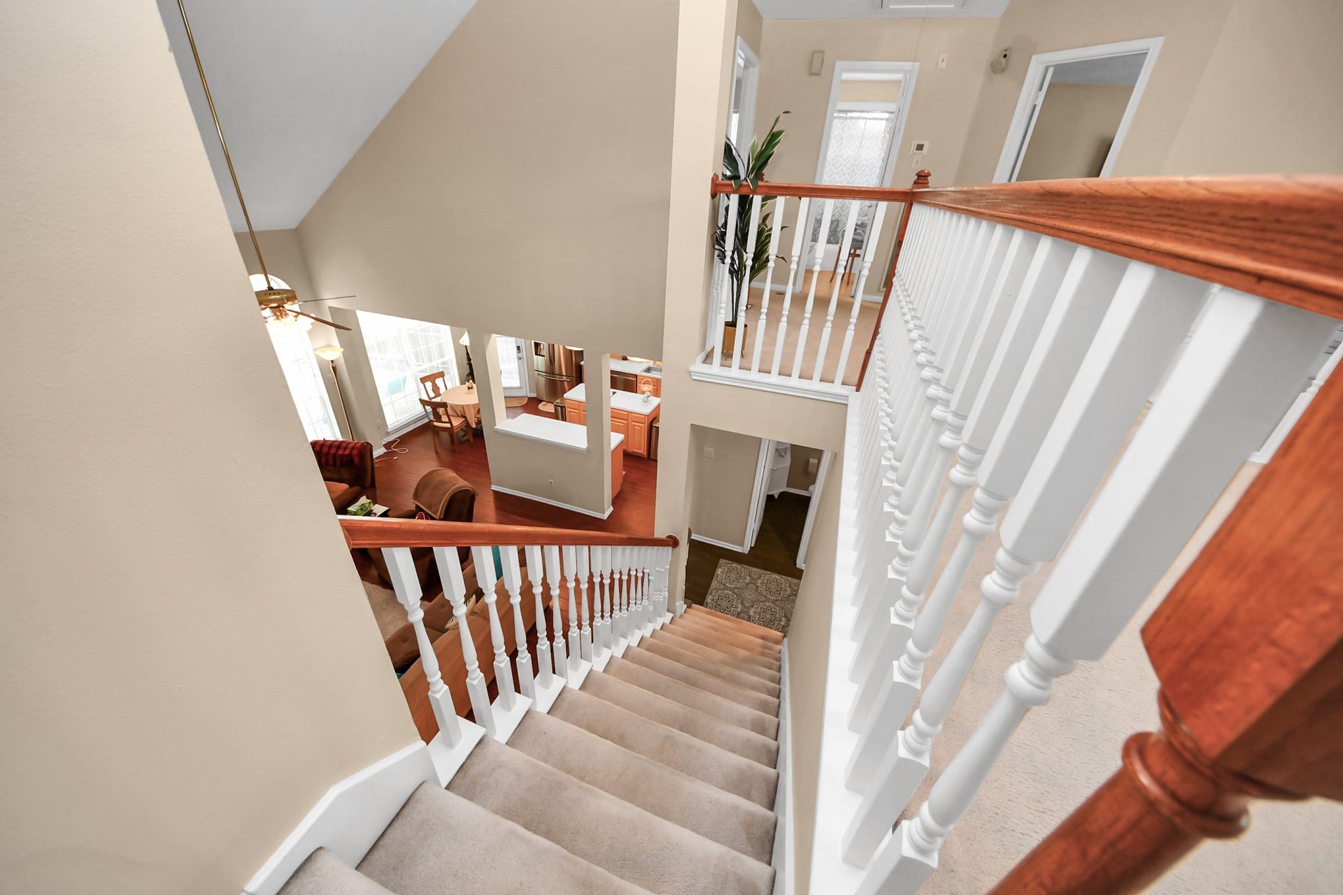 7015 Morningside Drive, Sugar Land, TX 77479 Elegant staircase with wooden handrails leads to an open, airy living space filled with natural light and a view of the dining and kitchen areas.