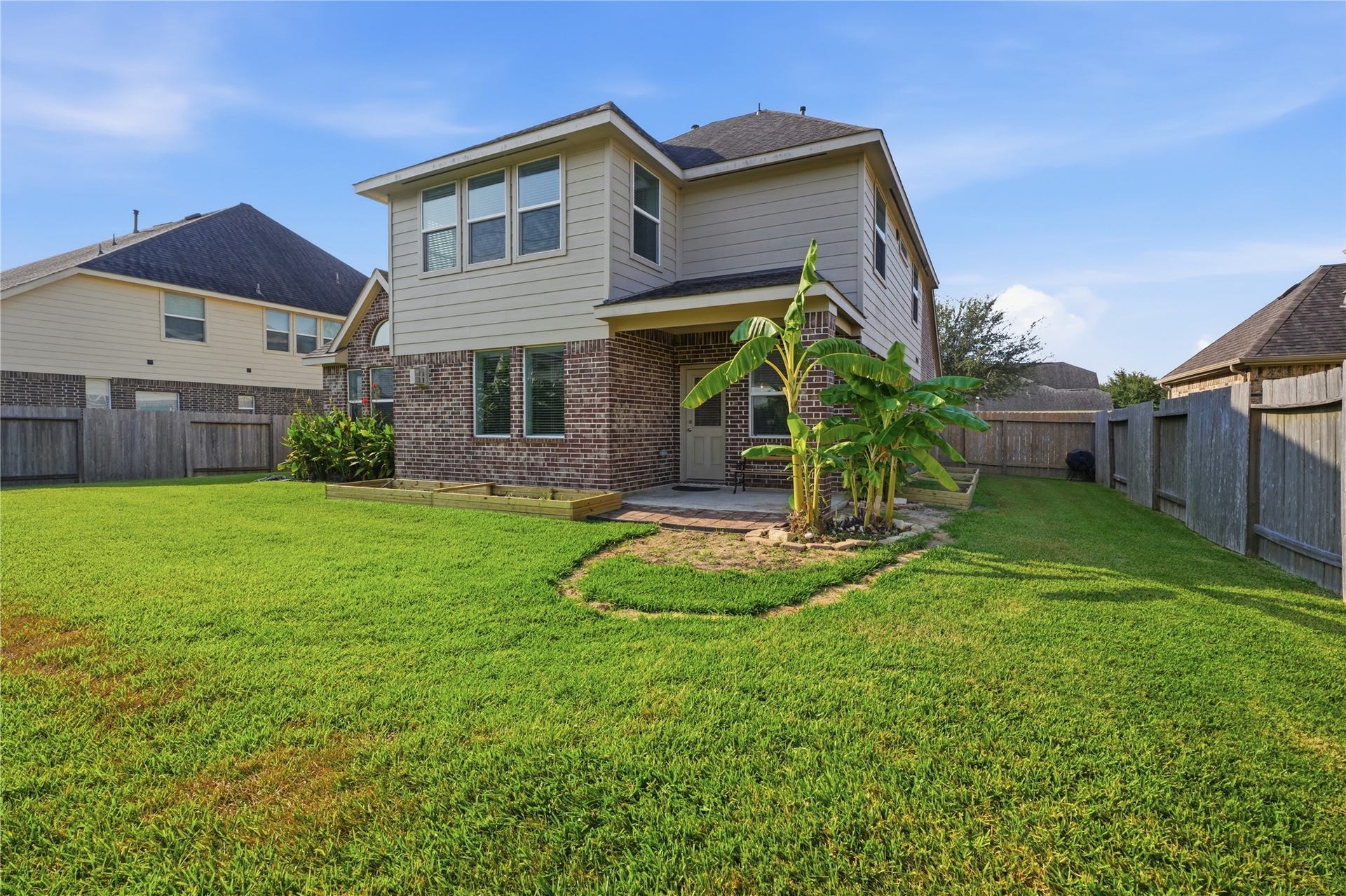 1717 Oakdale Mist Drive, Dickinson, TX 77539 Rear view of the home showcases the covered patio, expansive fenced yard, and freshly prepared garden beds along the back of the home.