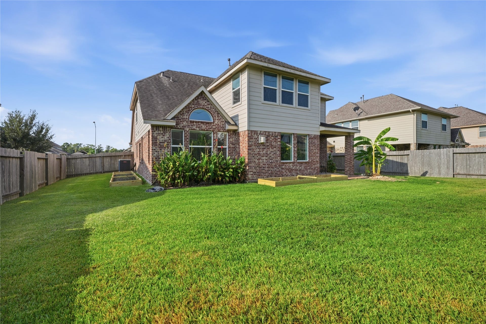 1717 Oakdale Mist Drive, Dickinson, TX 77539 Spacious fenced backyard with a large grassy area, mature landscaping, and freshly prepared garden beds ready for planting.