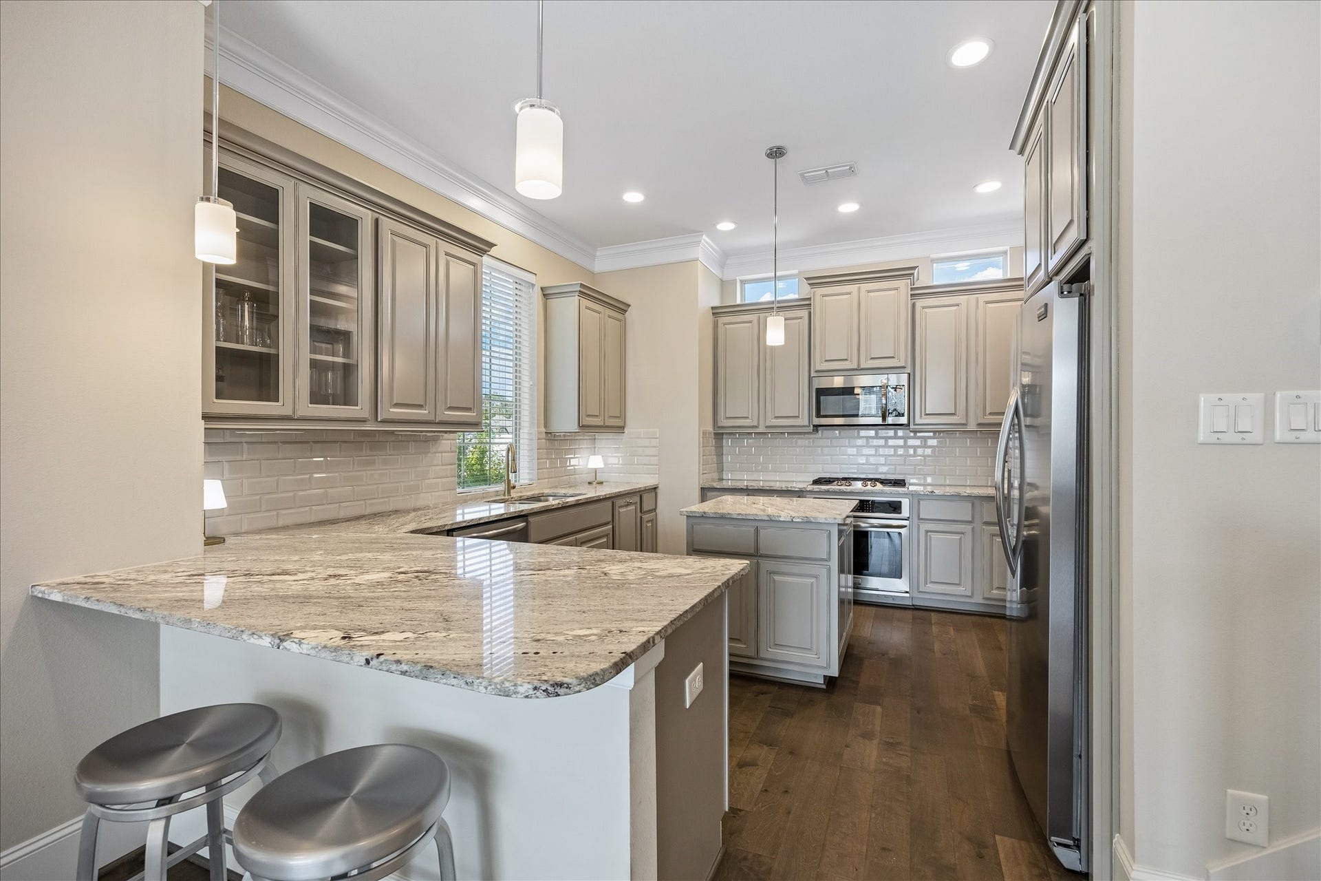 Gorgeous fully equipped kitchen featuring beautiful granite countertops, subway tile backsplash, abundant cabinetry & stainless steel Frigidaire appliances! Spacious island w/ granite countertop, built-in storage & breakfast bar seating creates a wonderful gathering space. Decorative pendant lighting & glass-front display cabinets enhance the timeless design. Seamlessly opens to dining & living areas; ideal for everyday living & entertaining!