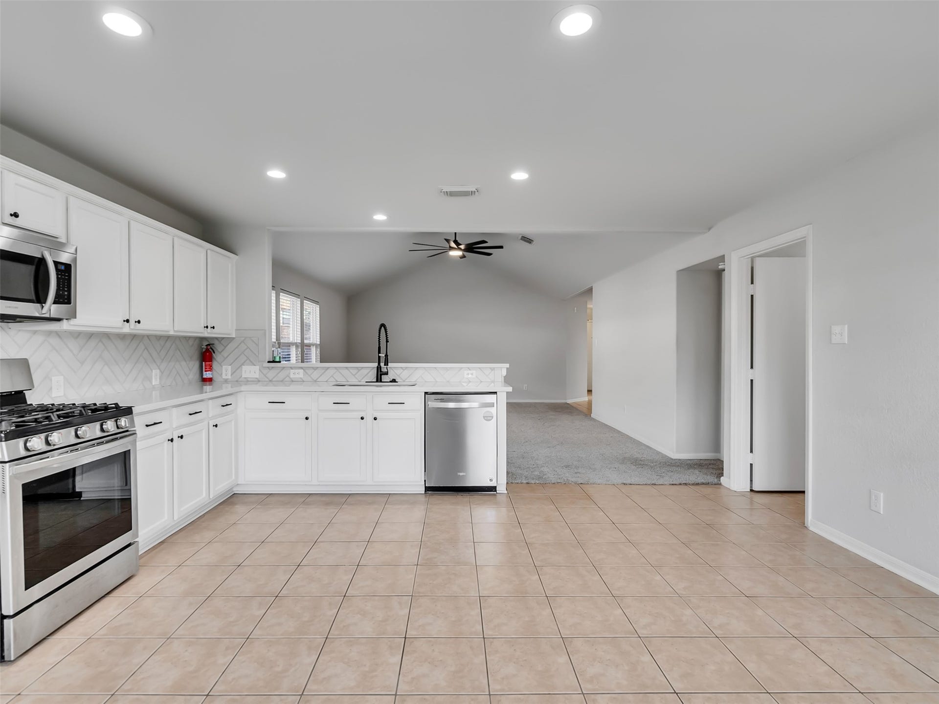 21518 Gannet Peak Way, Katy, TX 77449 This open-concept kitchen features modern stainless steel appliances, white cabinetry, and a stylish tile backsplash. The space flows seamlessly into a carpeted living area, enhanced by recessed lighting and a ceiling fan, creating a bright and inviting atmosphere.