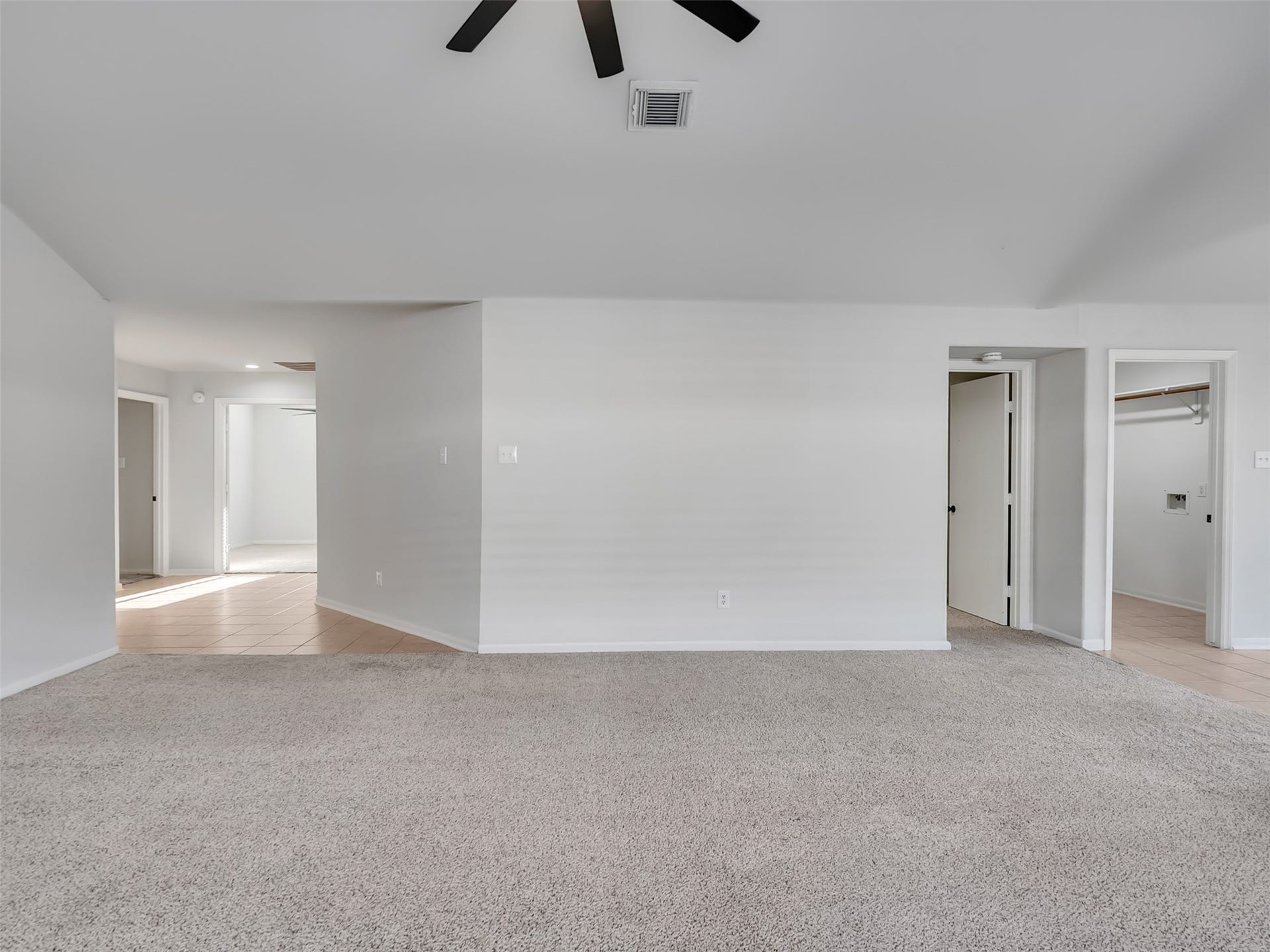 21518 Gannet Peak Way, Katy, TX 77449 This spacious room features neutral carpeting and walls, a ceiling fan for comfort, and multiple doorways leading to different areas of the home, offering versatile living options.