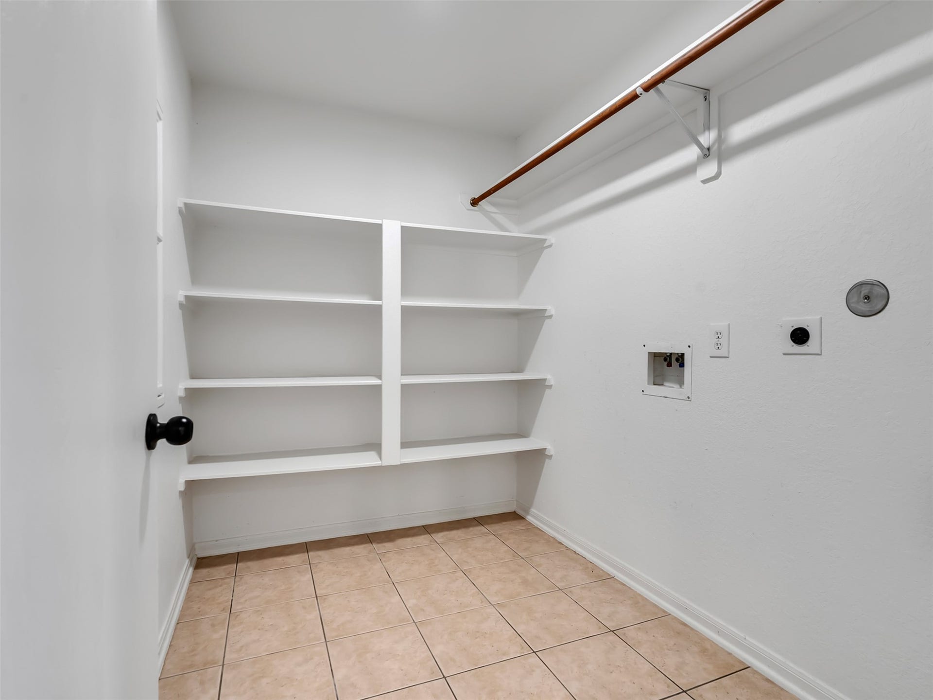 21518 Gannet Peak Way, Katy, TX 77449 A spacious laundry room with tiled flooring, white walls, built-in shelving, and hooks for hanging items. The room includes connections for a washer and dryer.