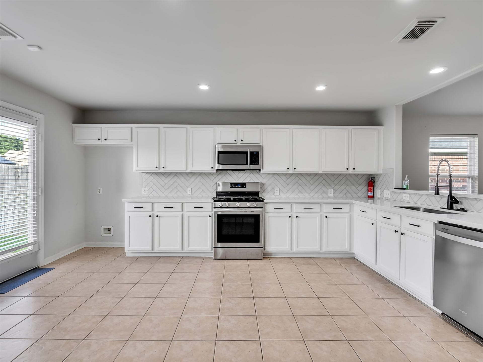 21518 Gannet Peak Way, Katy, TX 77449 This kitchen features modern stainless steel appliances, white cabinetry, a herringbone tile backsplash, and a spacious layout with large windows for natural light.