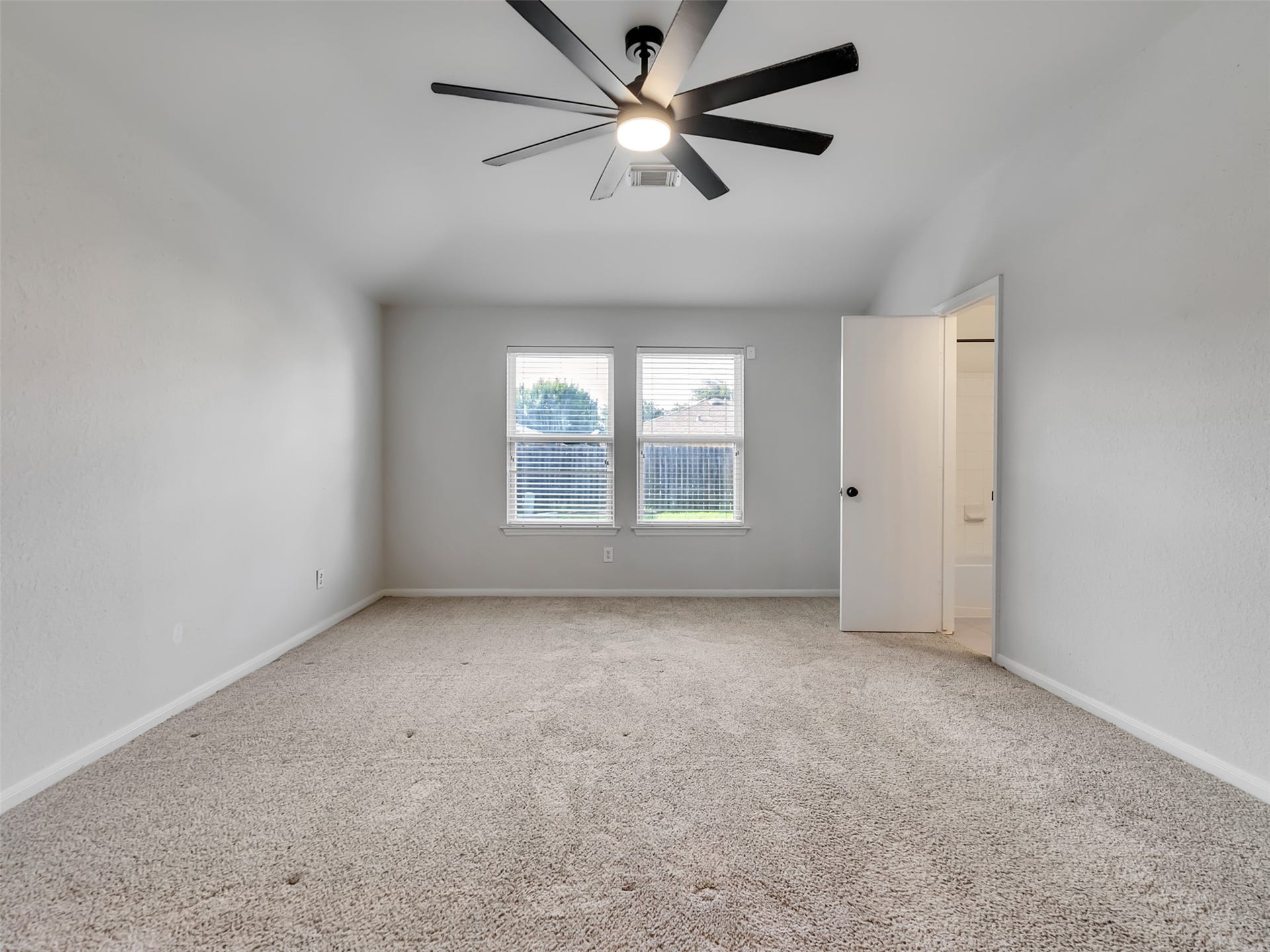 21518 Gannet Peak Way, Katy, TX 77449 This spacious bedroom features neutral carpeting, soft gray walls, and a modern ceiling fan. Natural light streams in through two windows, and an adjacent door leads to a bathroom, adding convenience and privacy.