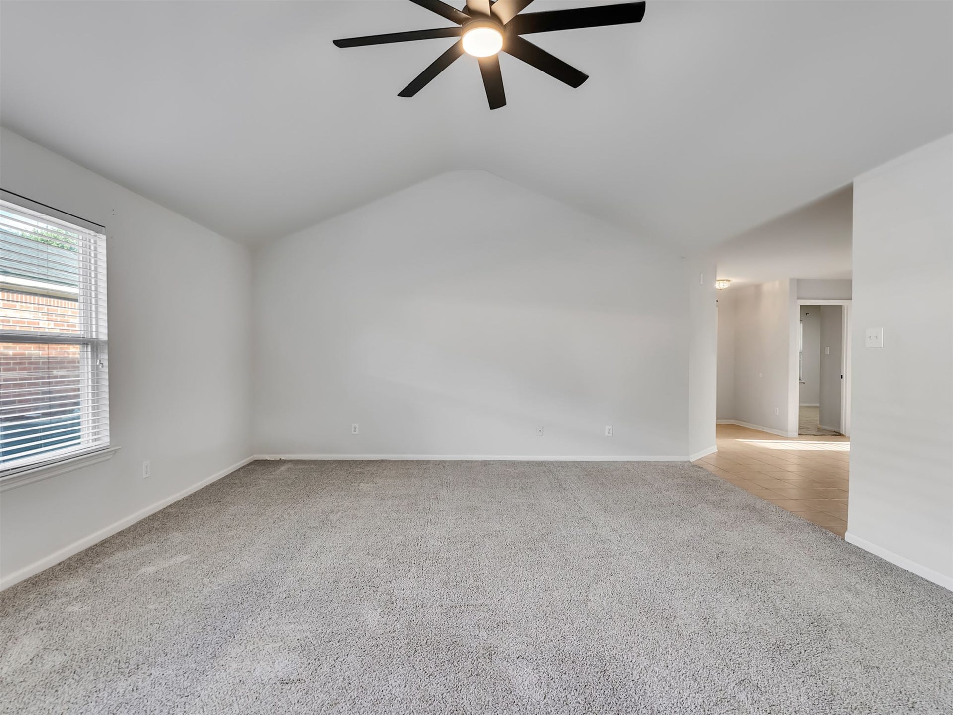 21518 Gannet Peak Way, Katy, TX 77449 This spacious room features neutral walls and carpet, a large window for natural light, and a modern ceiling fan. It leads into a tiled hallway, providing a clean and open feel.