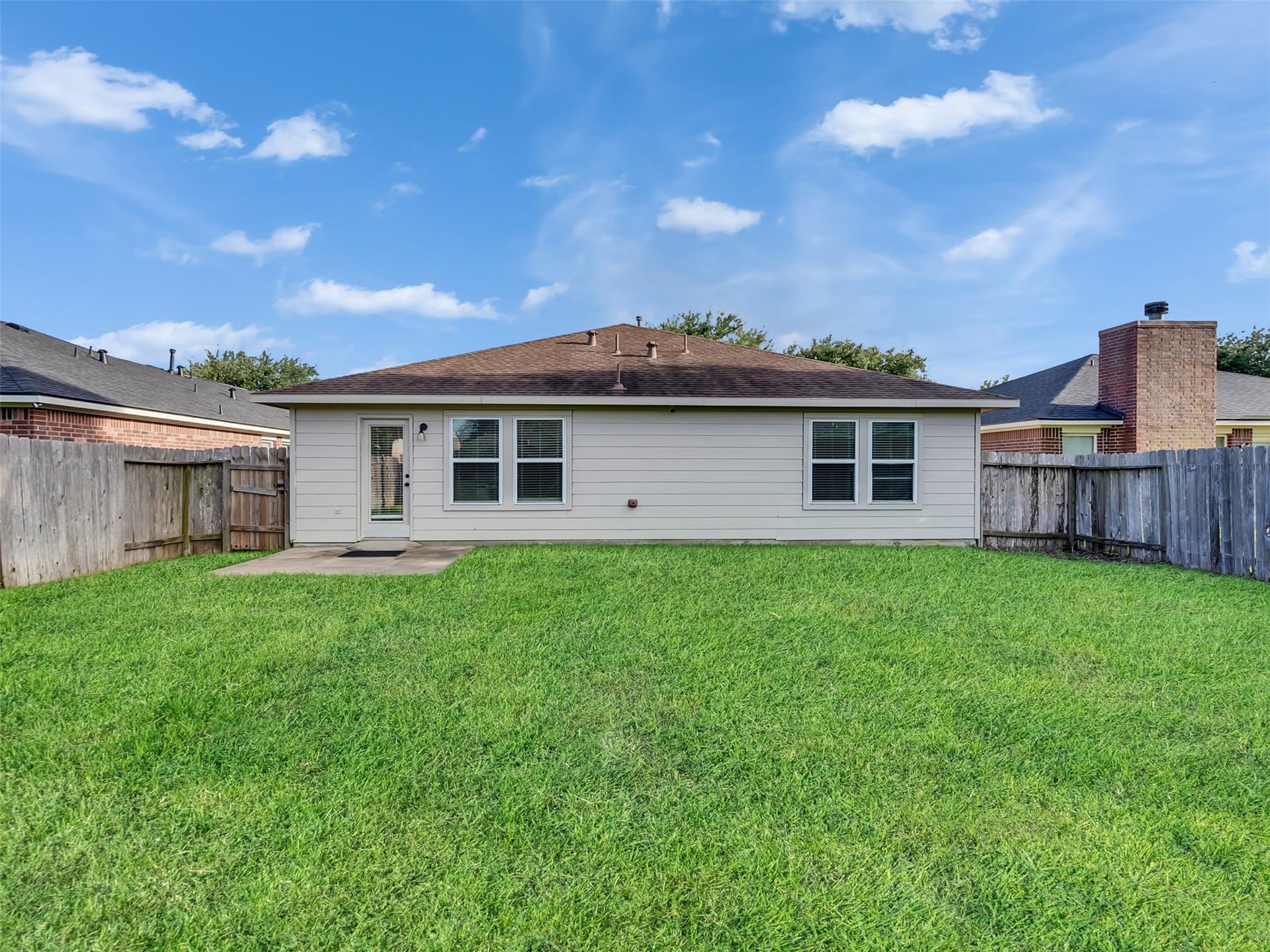 21518 Gannet Peak Way, Katy, TX 77449 A spacious backyard with a well-maintained lawn, bordered by a wooden fence. The house has a simple, single-story exterior with a patio area and back door, offering a great space for outdoor activities.