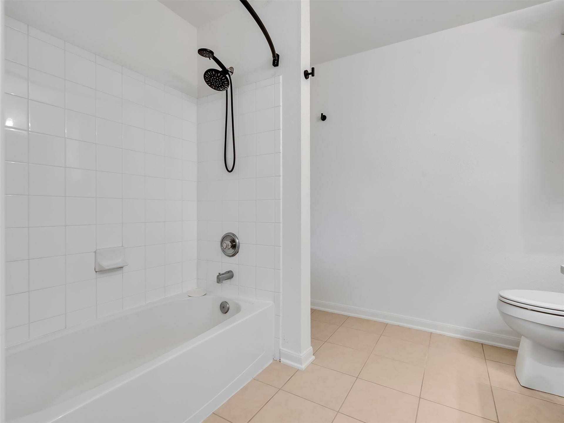 21518 Gannet Peak Way, Katy, TX 77449 This bathroom features a clean, minimalist design with a tiled bathtub and shower area, modern fixtures, and a toilet, all set against neutral-colored walls and floor tiles.