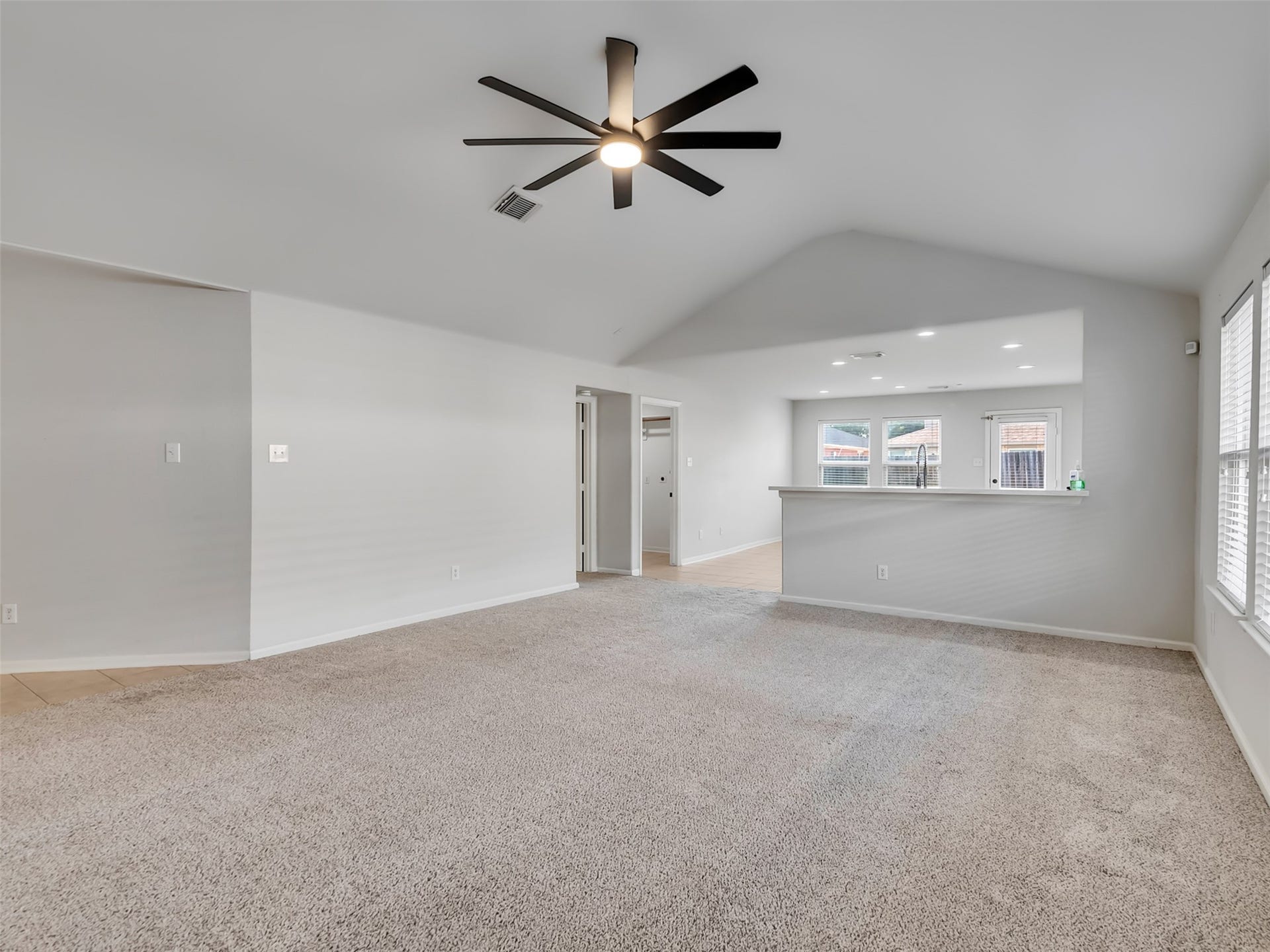 21518 Gannet Peak Way, Katy, TX 77449 This spacious living area features plush carpeting, a modern ceiling fan, and abundant natural light from large windows. The open layout seamlessly connects to a kitchen area, perfect for entertaining.