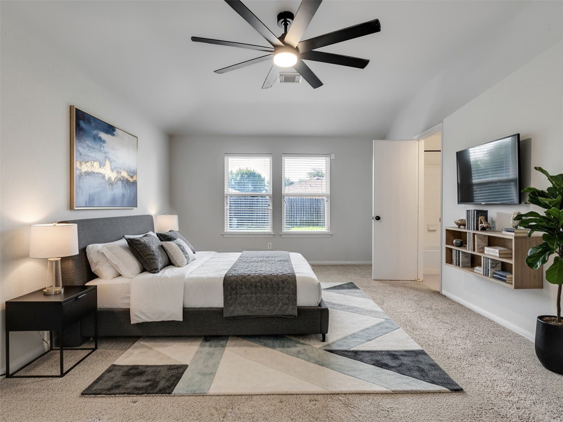 21518 Gannet Peak Way, Katy, TX 77449 Spacious master bedroom with neutral tones, featuring a modern ceiling fan, large windows for natural light, and an en-suite bathroom. The room includes a cozy bed, stylish artwork, and a mounted TV with shelving for storage.