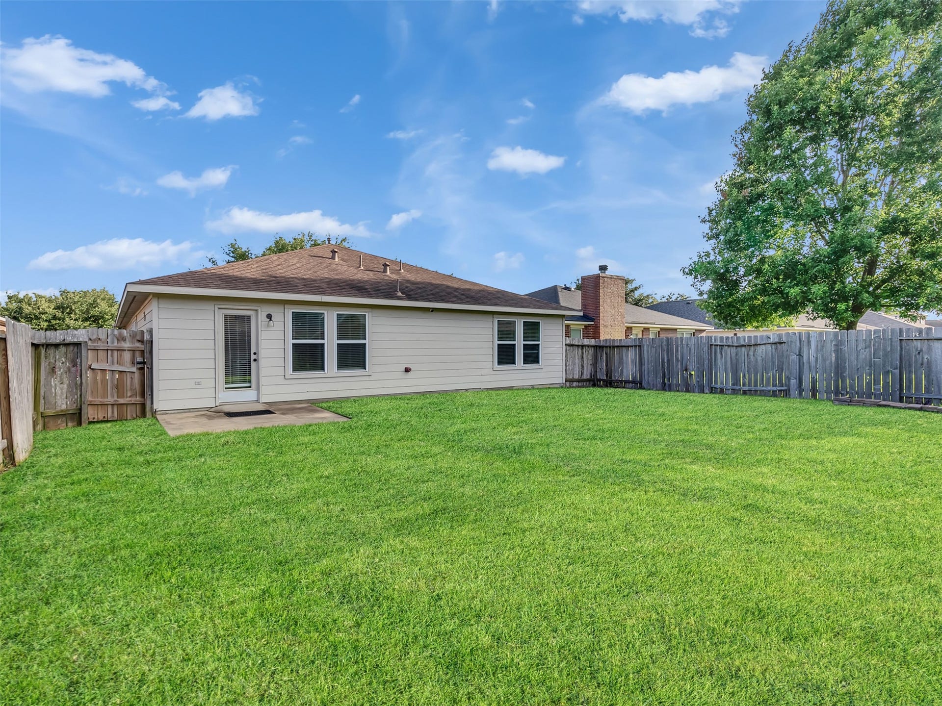 21518 Gannet Peak Way, Katy, TX 77449 Spacious backyard with well-maintained lawn, fenced for privacy. The single-story house features a light exterior and several windows, allowing for natural light. Ideal for outdoor activities and family gatherings.