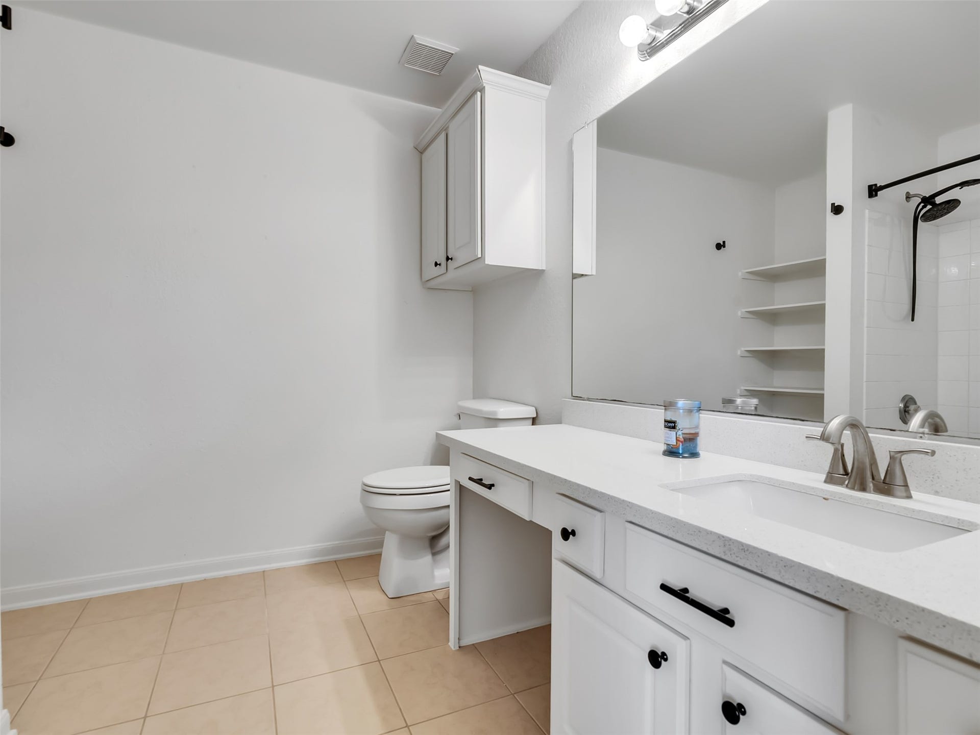 21518 Gannet Peak Way, Katy, TX 77449 Modern bathroom with a large mirror, white cabinetry, and ample counter space. Features a shower-tub combo and open shelving for storage. Bright lighting and neutral tiles create a clean, fresh look.