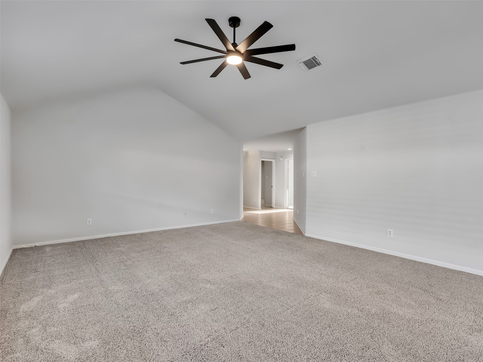 21518 Gannet Peak Way, Katy, TX 77449 Spacious, carpeted room with a vaulted ceiling and modern ceiling fan. Neutral walls enhance the open feel, leading to a hallway with natural light. Ideal for a living area or large bedroom.