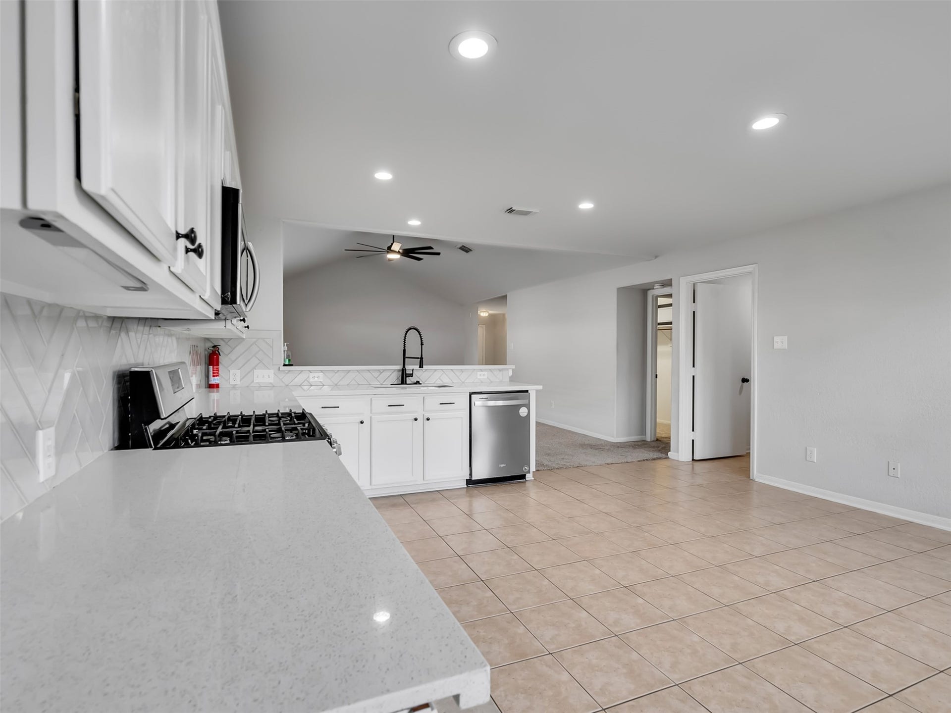 21518 Gannet Peak Way, Katy, TX 77449 Bright, open-concept kitchen with modern appliances, white cabinetry, and a sleek backsplash. The space flows into a tiled living area with recessed lighting and a ceiling fan, ideal for entertaining.