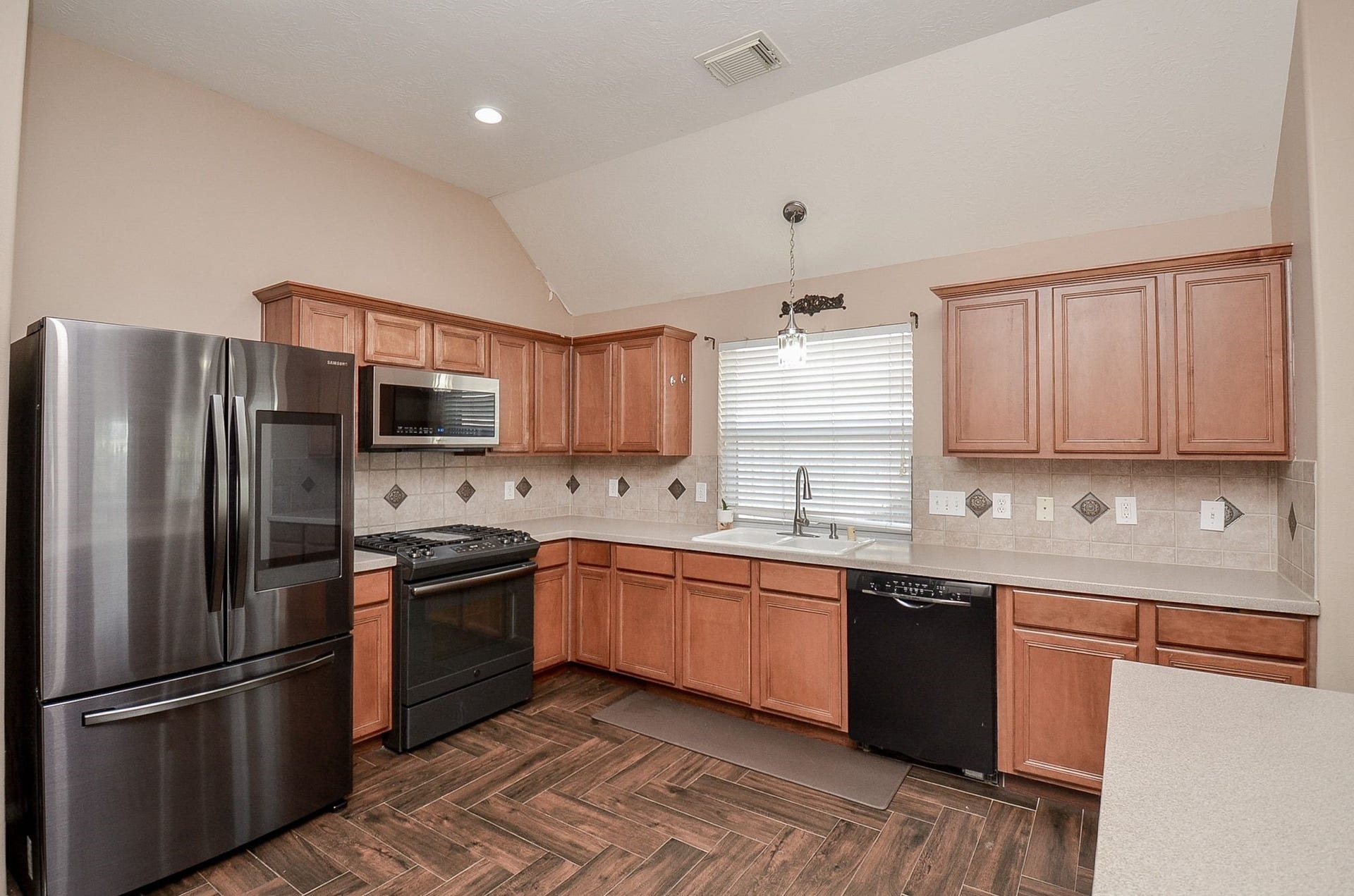 3706 Cane Lake Drive, Richmond, TX 77406 Spacious kitchen featuring sleek stainless steel appliances, warm wood cabinetry, and elegant tile backsplash, complemented by rich wood tile flooring and ample counter space.