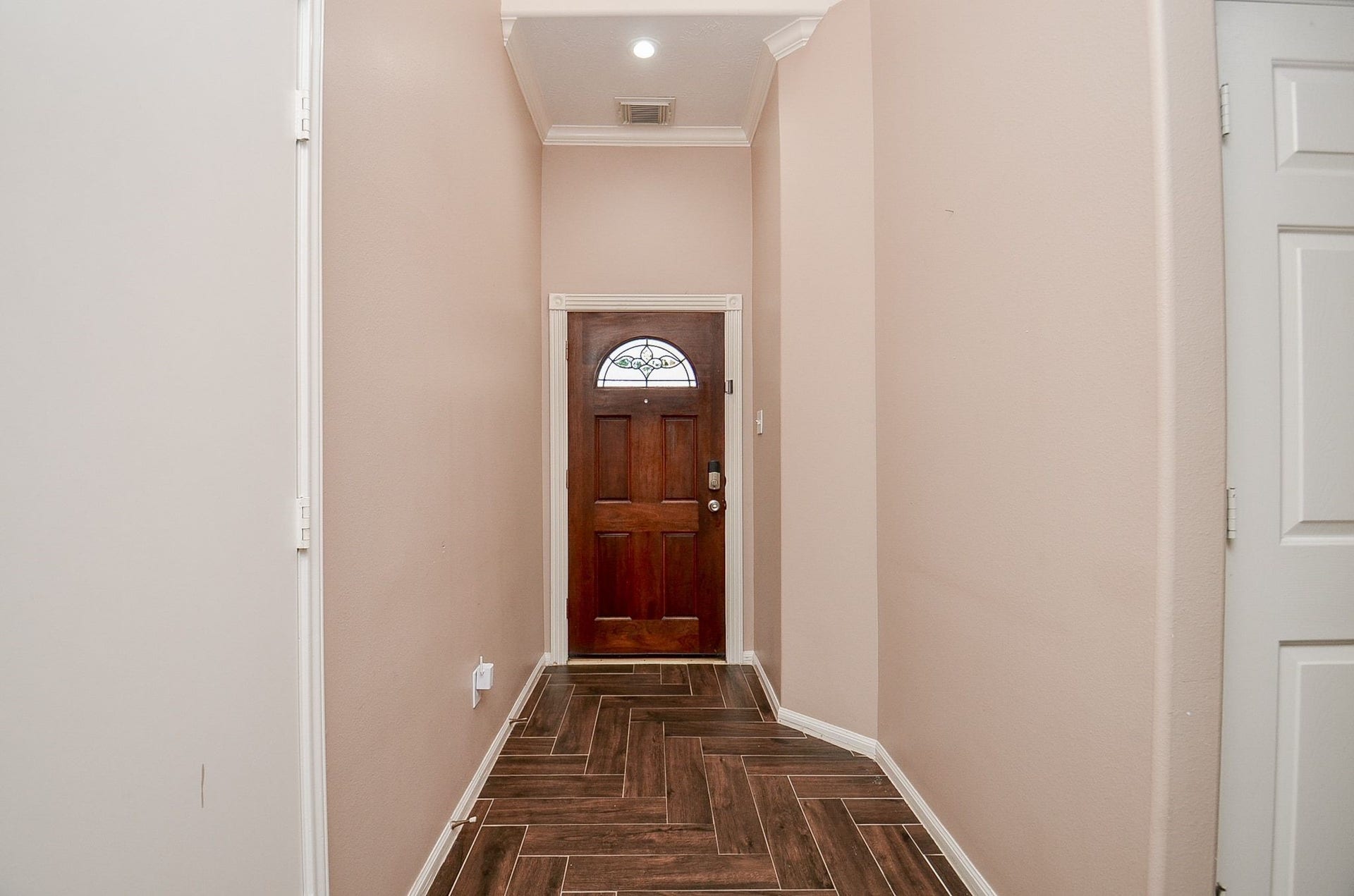 3706 Cane Lake Drive, Richmond, TX 77406 Inviting entryway with warm-toned walls, elegant crown molding, and stylish wood-look tile flooring leading to a charming wooden front door.