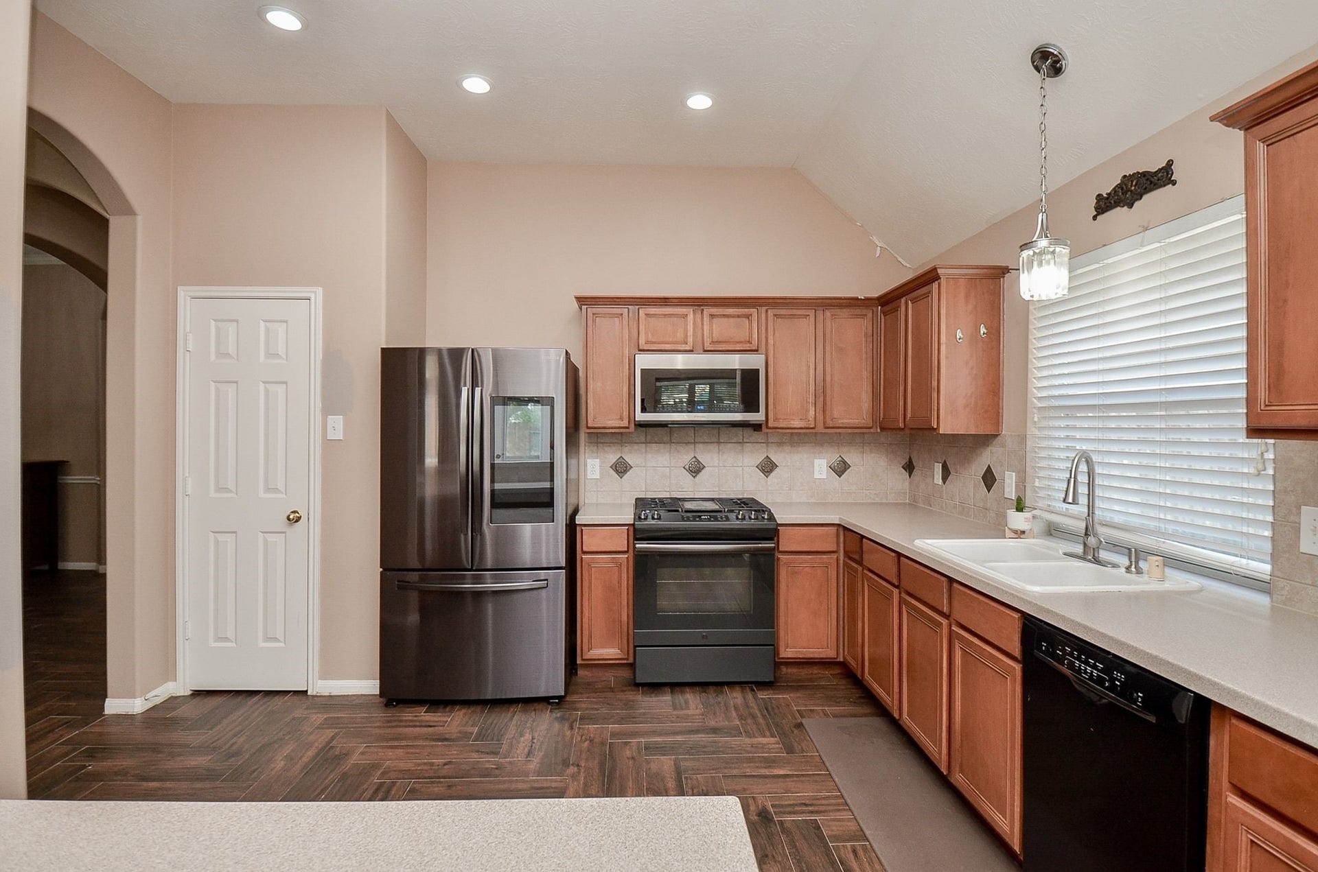 3706 Cane Lake Drive, Richmond, TX 77406 Spacious kitchen with stainless steel appliances, ample wooden cabinetry, and elegant tile backsplash. The large window provides plenty of natural light, complemented by recessed ceiling lighting.