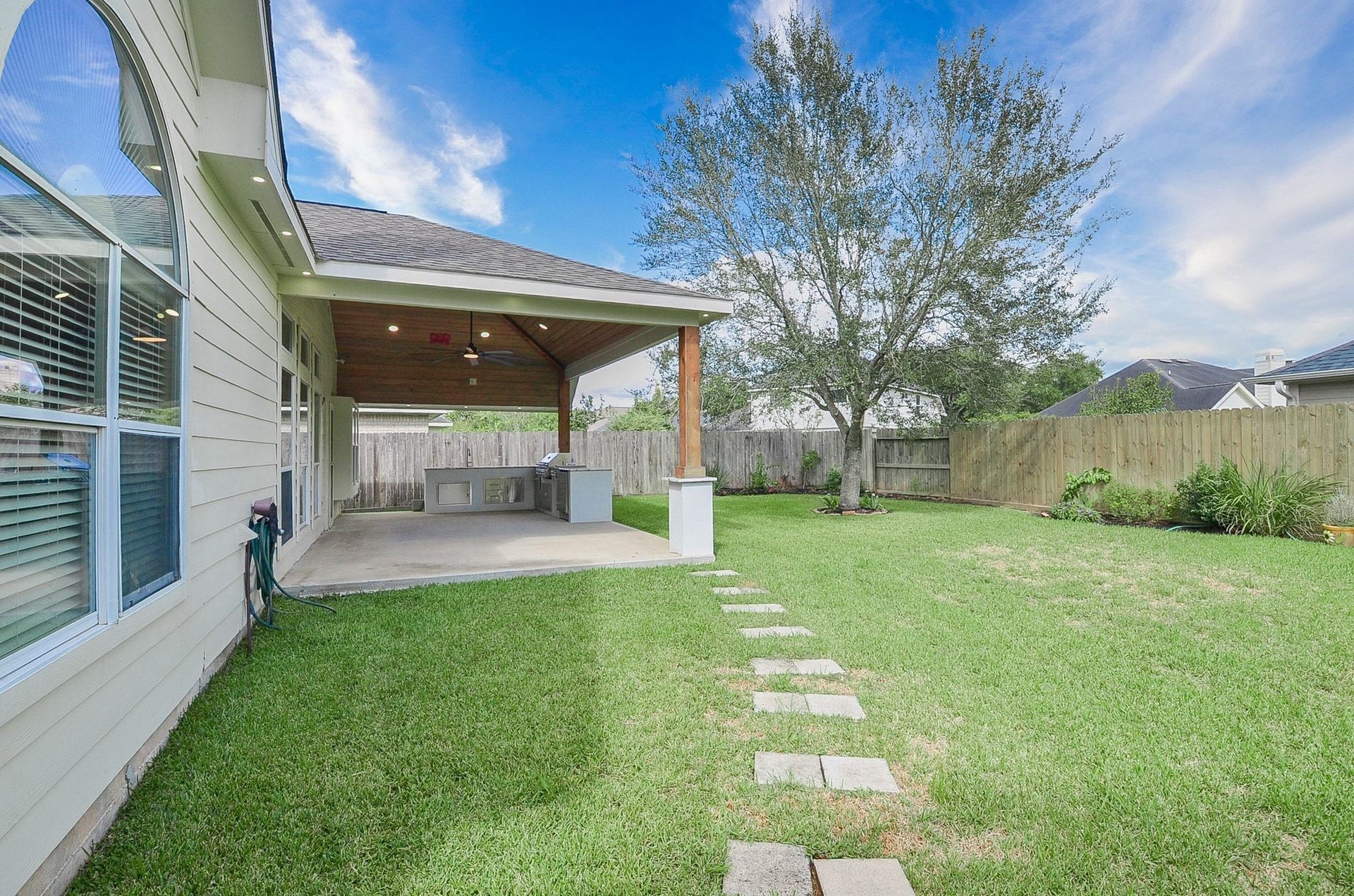 3706 Cane Lake Drive, Richmond, TX 77406 Spacious backyard featuring a covered patio with an outdoor kitchen, perfect for entertaining, surrounded by a lush lawn and mature tree for added privacy.