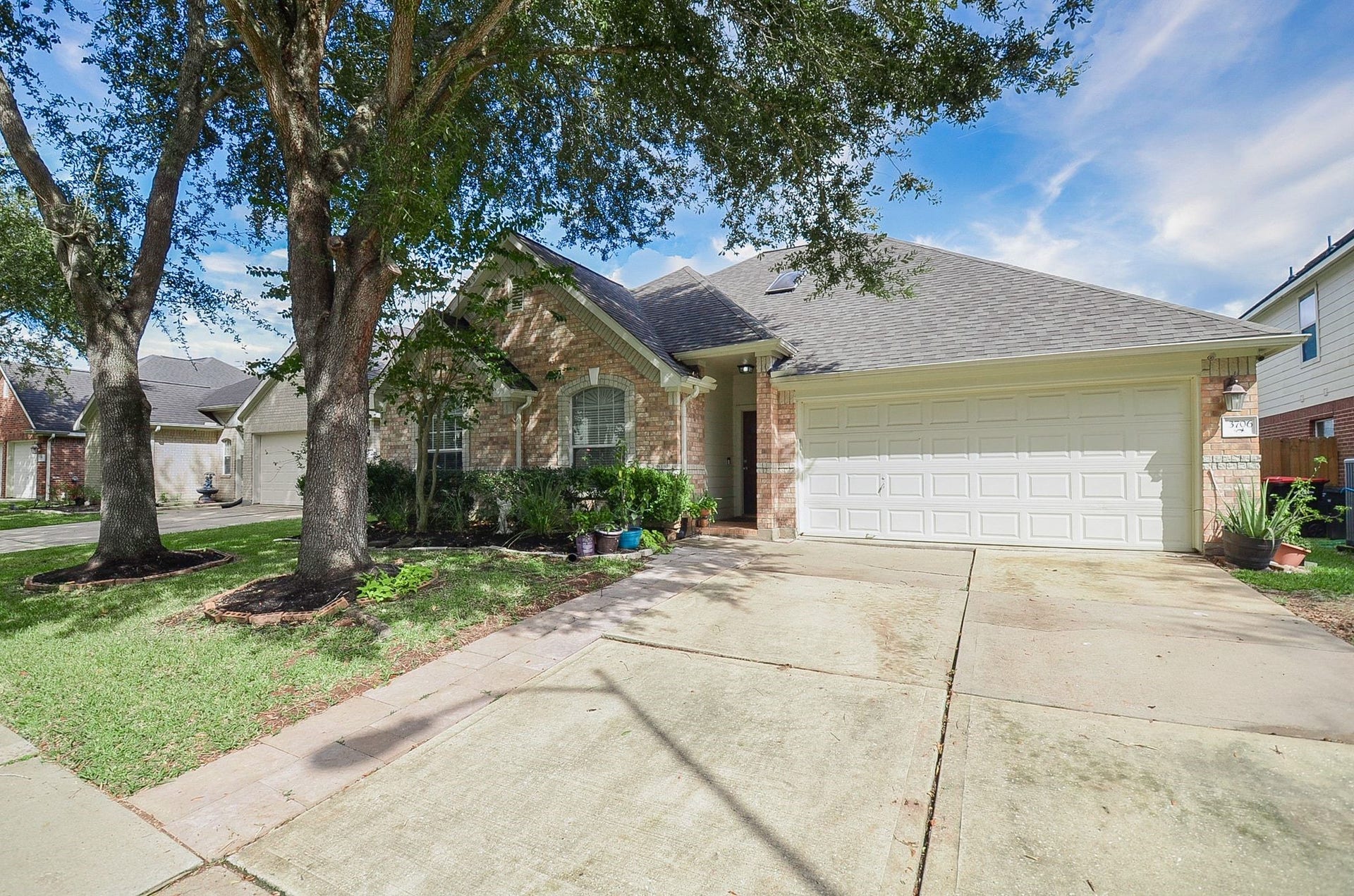3706 Cane Lake Drive, Richmond, TX 77406 Charming brick home with a spacious two-car garage, nestled under mature trees, offering a welcoming front yard and inviting curb appeal.