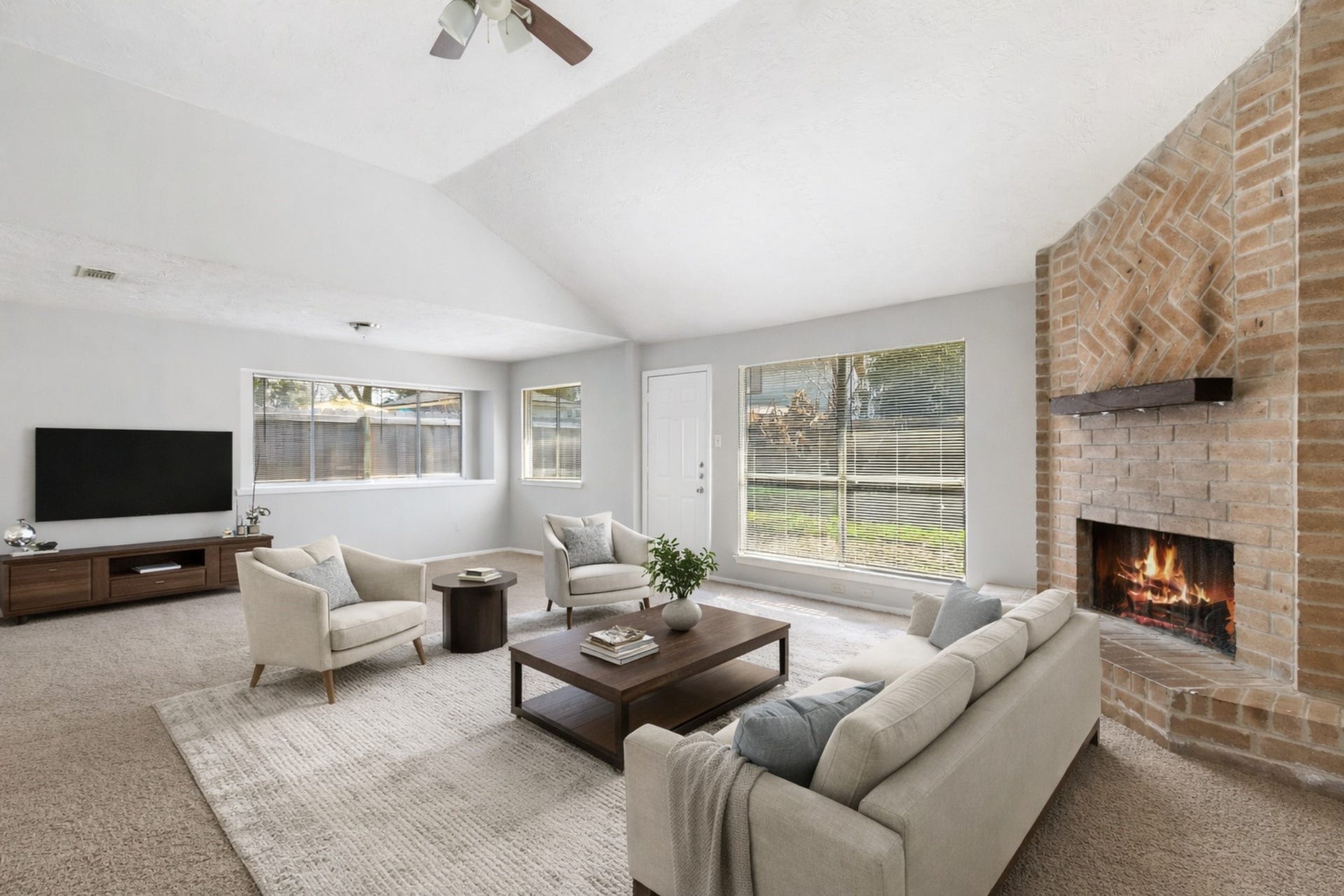 Spacious living room with vaulted ceilings, abundant natural light, and a striking brick fireplace, virtually staged to showcase a comfortable seating arrangement and inviting layout ideal for both relaxing and entertaining