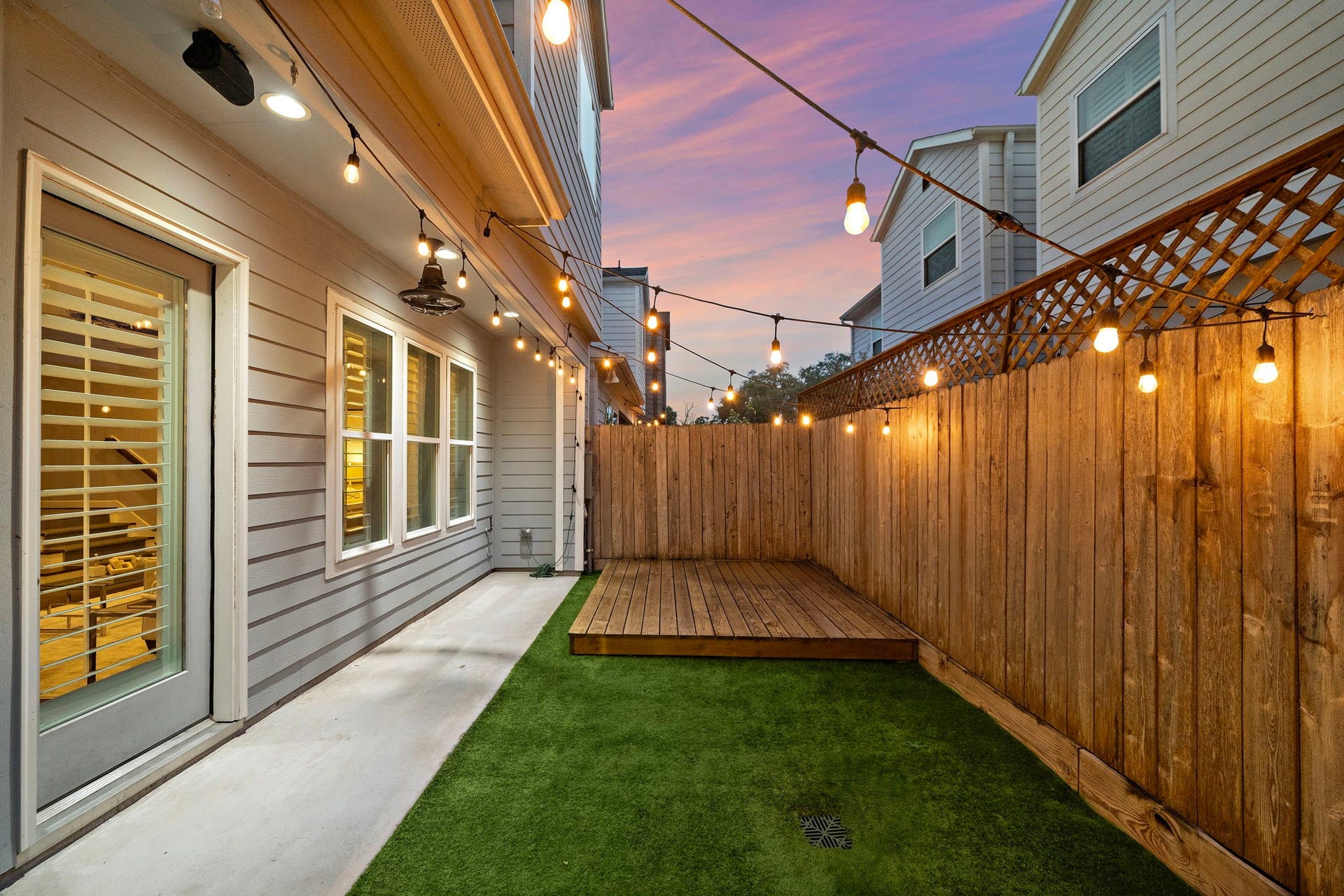 4926 Ella Boulevard, Houston, TX 77018 This cozy backyard features a wooden deck, artificial grass, and warm string lights, perfect for evening relaxation or small gatherings. The fenced area provides privacy, and the modern exterior complements the inviting atmosphere.