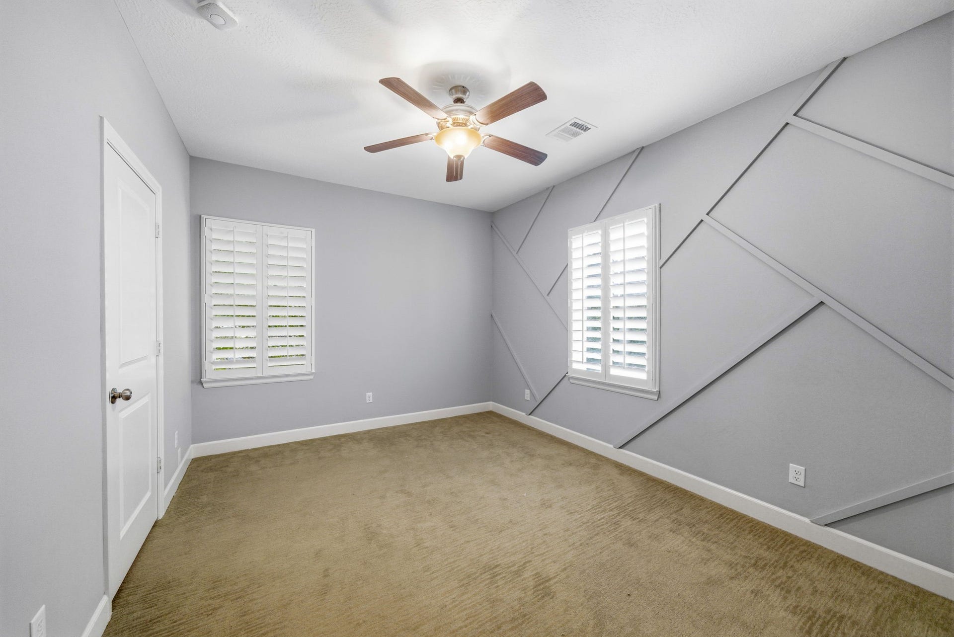 4926 Ella Boulevard, Houston, TX 77018 Bright and spacious bedroom featuring a modern geometric accent wall, neutral carpeting, and white shutters on the windows. A ceiling fan provides comfort and light. Large closet with Custom Elfa closet system.