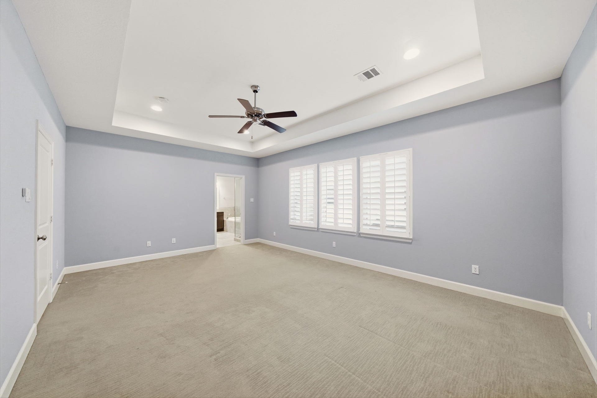 4926 Ella Boulevard, Houston, TX 77018 Spacious primary suite, tray ceiling, and a ceiling fan. The room features carpeted flooring, large windows with shutters, and an en-suite bathroom.